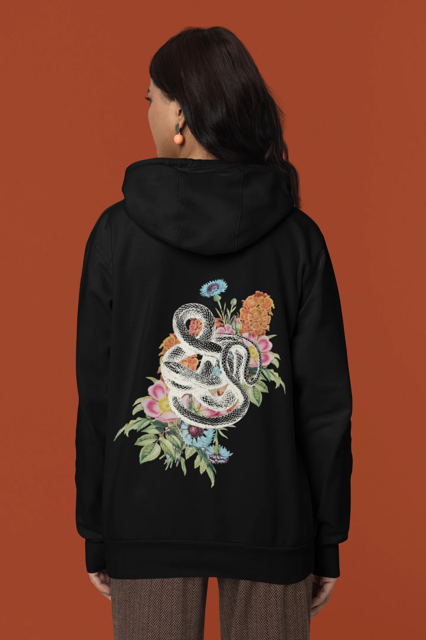 Back view of a female model wearing a black hoodie with a snake coiled around flowers, symbolizing the harmony between nature and its creatures.