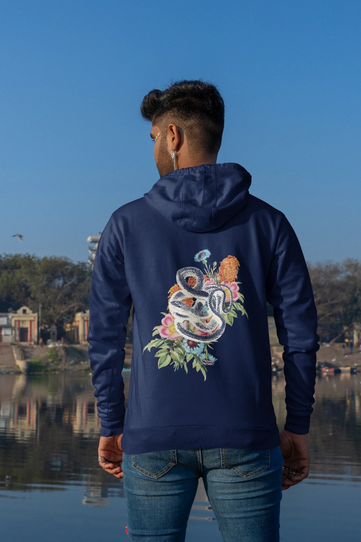 Back of male model wearing a navy blue hoodie with a snake coiled around flowers, symbolizing the harmony between nature and its creatures.