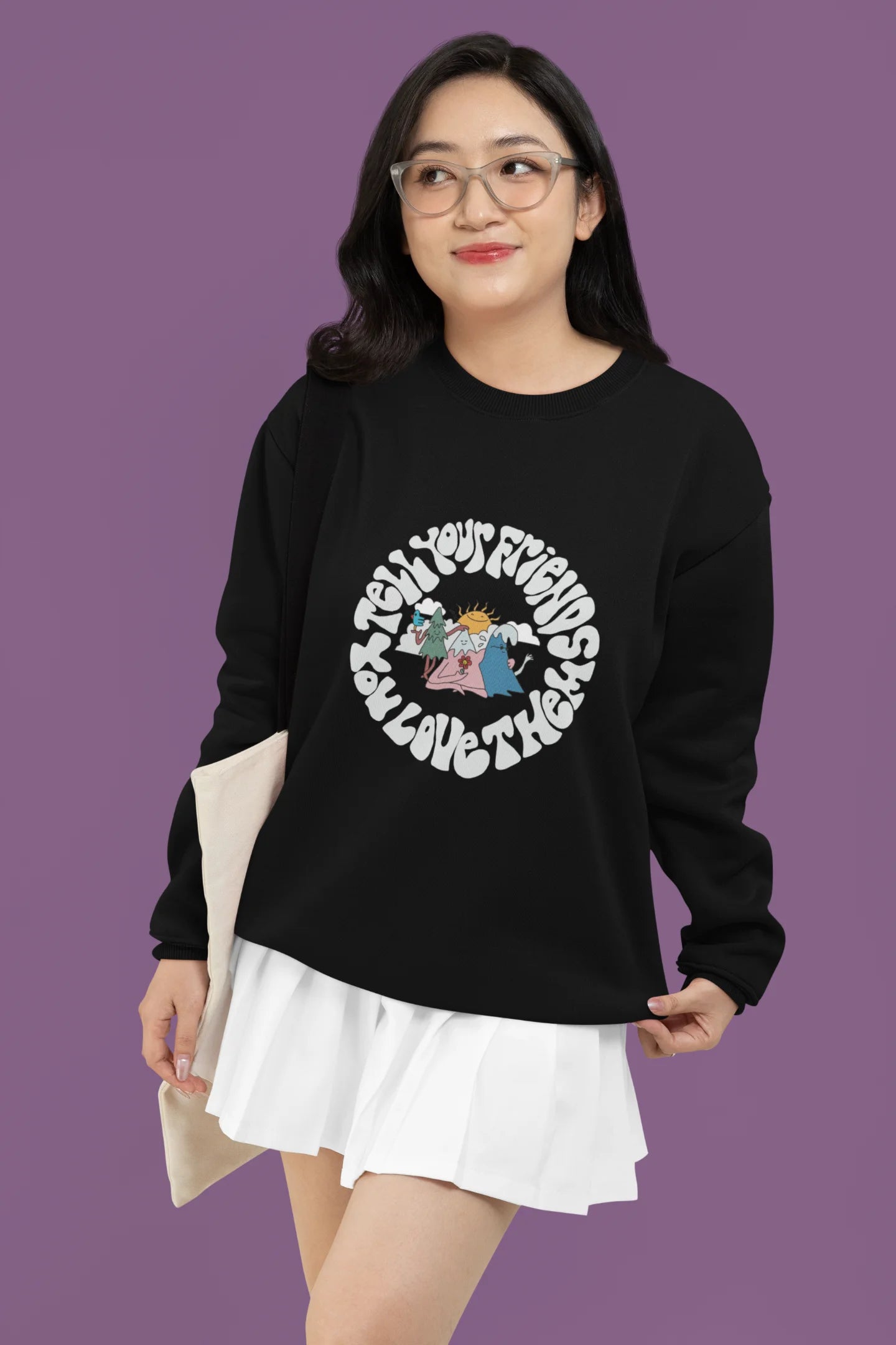 First front view of a female model wearing a black sweatshirt with a design of smiling mountains and a sunrise, and the text "Tell Your Friends You Love Them."