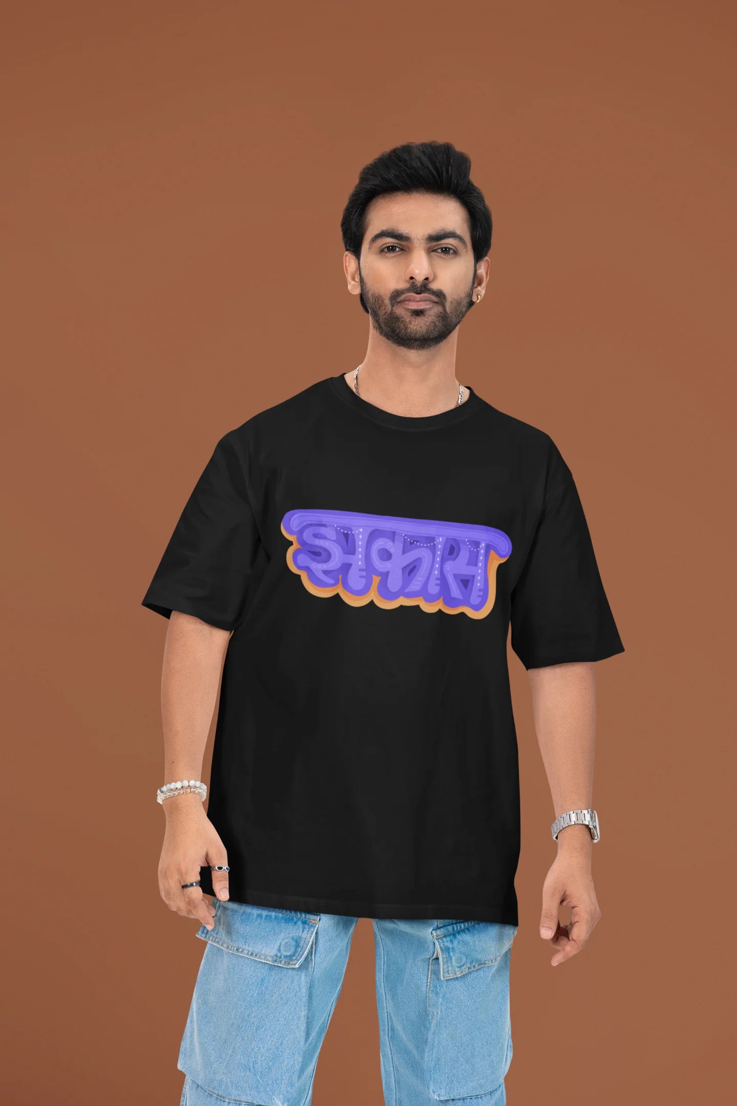 First front view of a male model wearing an black oversized t-shirt featuring "Jhakas" in a stylish font.