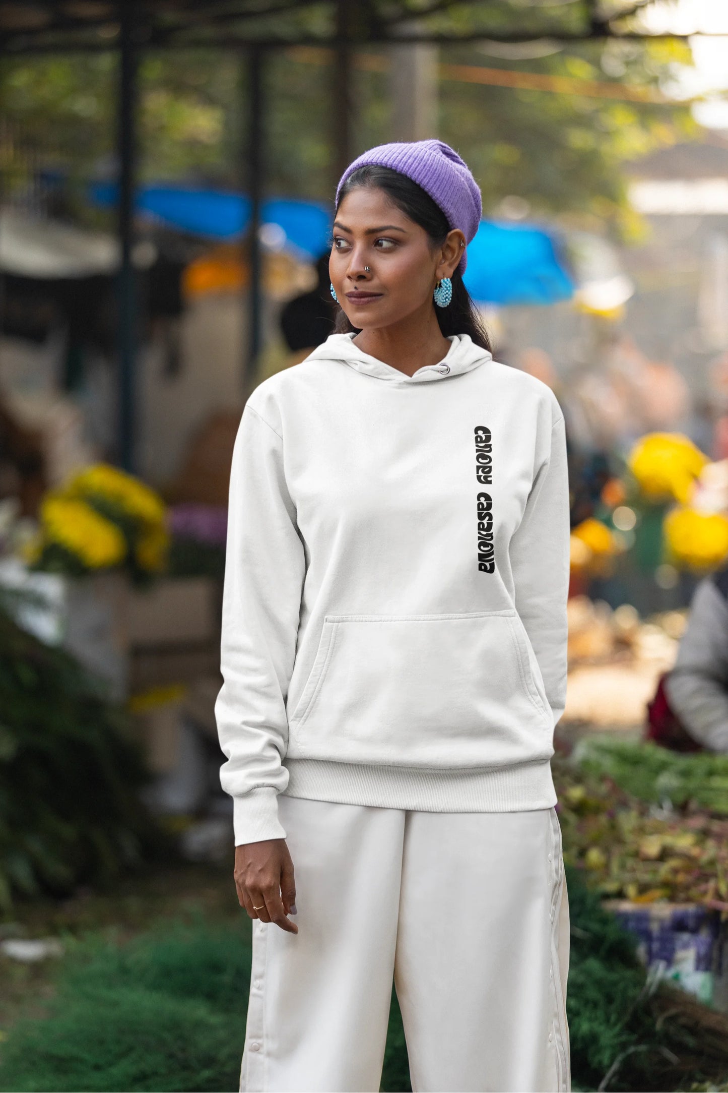 First front view of a female model wearing a white hoodie with a toucan perched on a branch in a jungle setting.