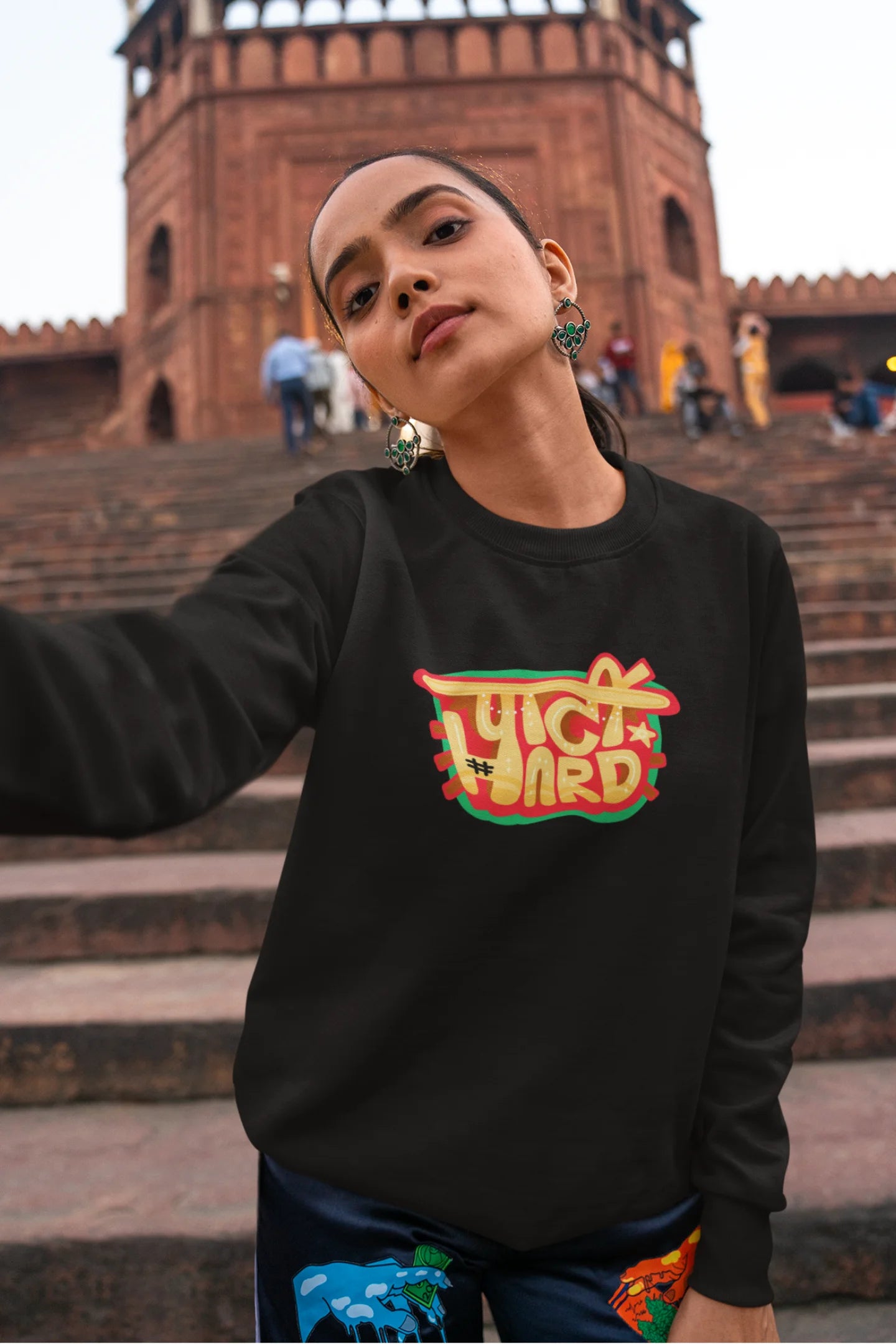 First front view of a female model wearing a black oversized t-shirt with the phrase "Party Hard" in an energetic Hindi.