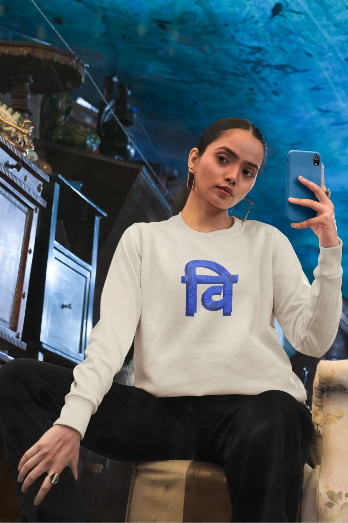 2nd front view of a female model wearing a cream sweatshirt with the phrase "Vichitra Pranee" (meaning "Strange being" or "alien") in a stylish Hindi font.