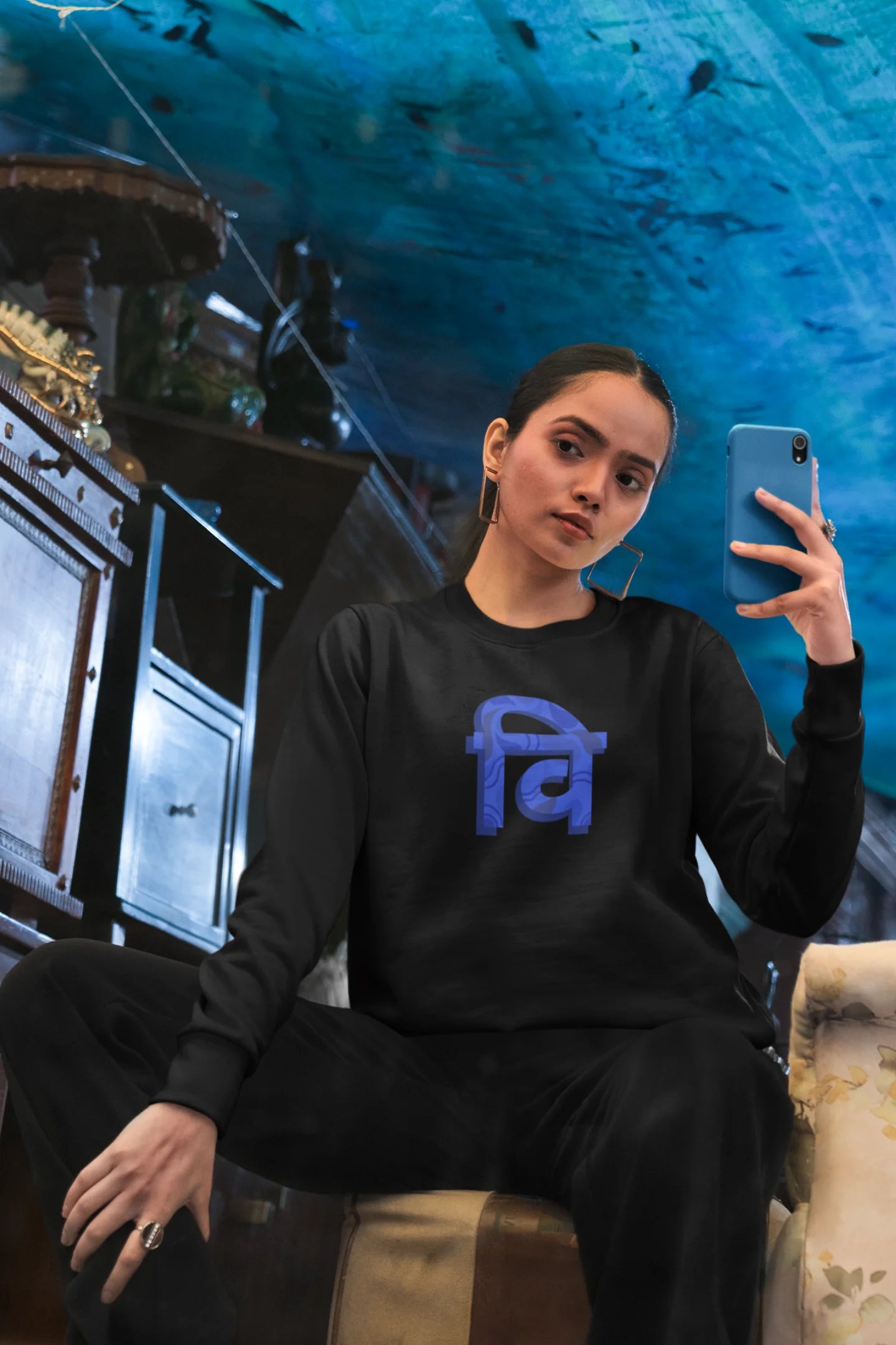 2nd front view of a female model wearing a black sweatshirt with the phrase "Vichitra Pranee" (meaning "Strange being" or "alien") in a stylish Hindi font.