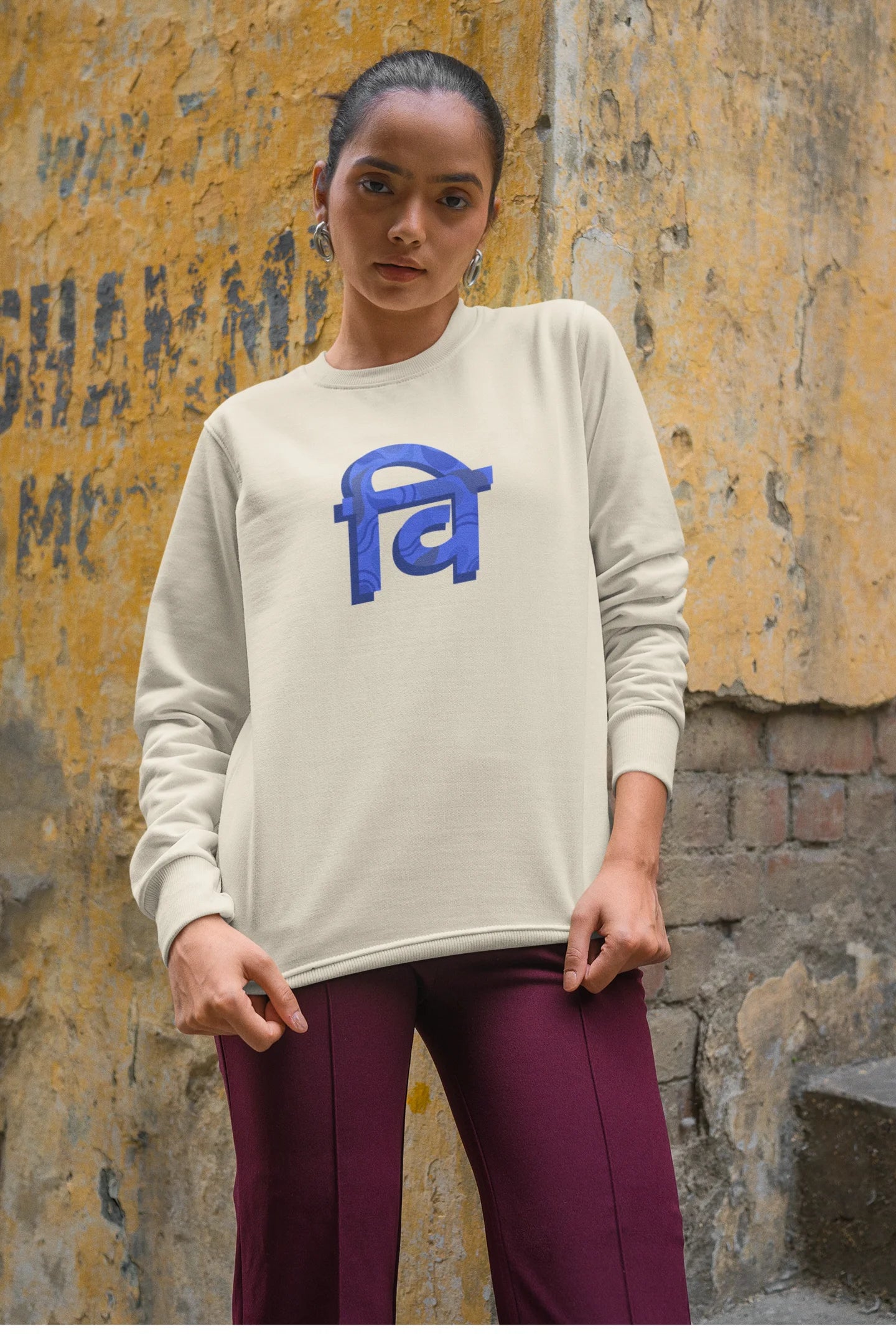 6th front view of a female model wearing a cream sweatshirt with the phrase "Vichitra Pranee" (meaning "Strange being" or "alien") in a stylish Hindi font.