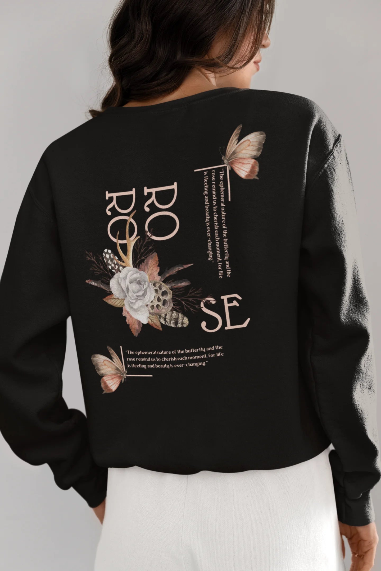 Back view of a female model wearing a black sweatshirt featuring a beautiful rose design with inspirational text, offering a calming and uplifting aesthetic.