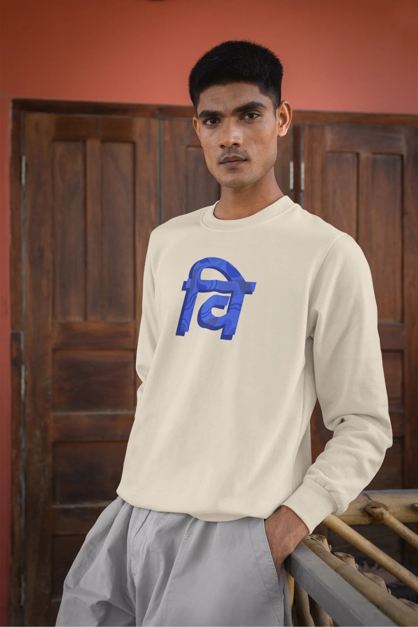 2nd front view of a male model wearing a cream sweatshirt with the phrase "Vichitra Pranee" (meaning "Strange being" or "alien") in a stylish Hindi font.