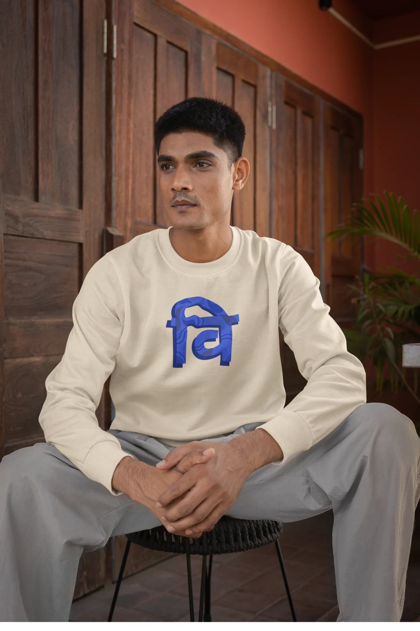 First front view of a male model wearing a cream sweatshirt with the phrase "Vichitra Pranee" (meaning "Strange being" or "alien") in a stylish Hindi font.