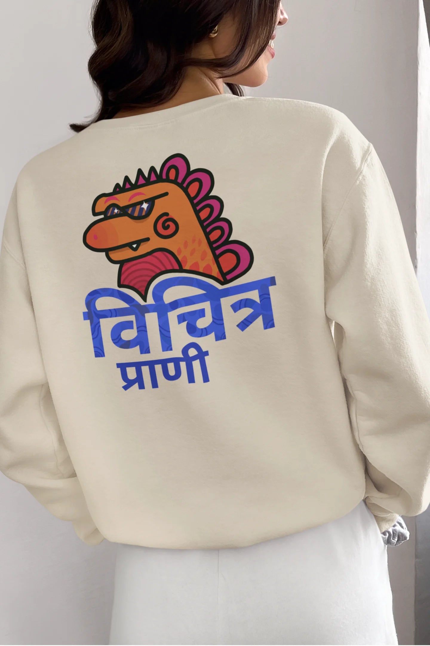 Back view of a female model wearing a cream sweatshirt with the phrase "Vichitra Pranee" (meaning "Strange being" or "alien") in a stylish Hindi font.