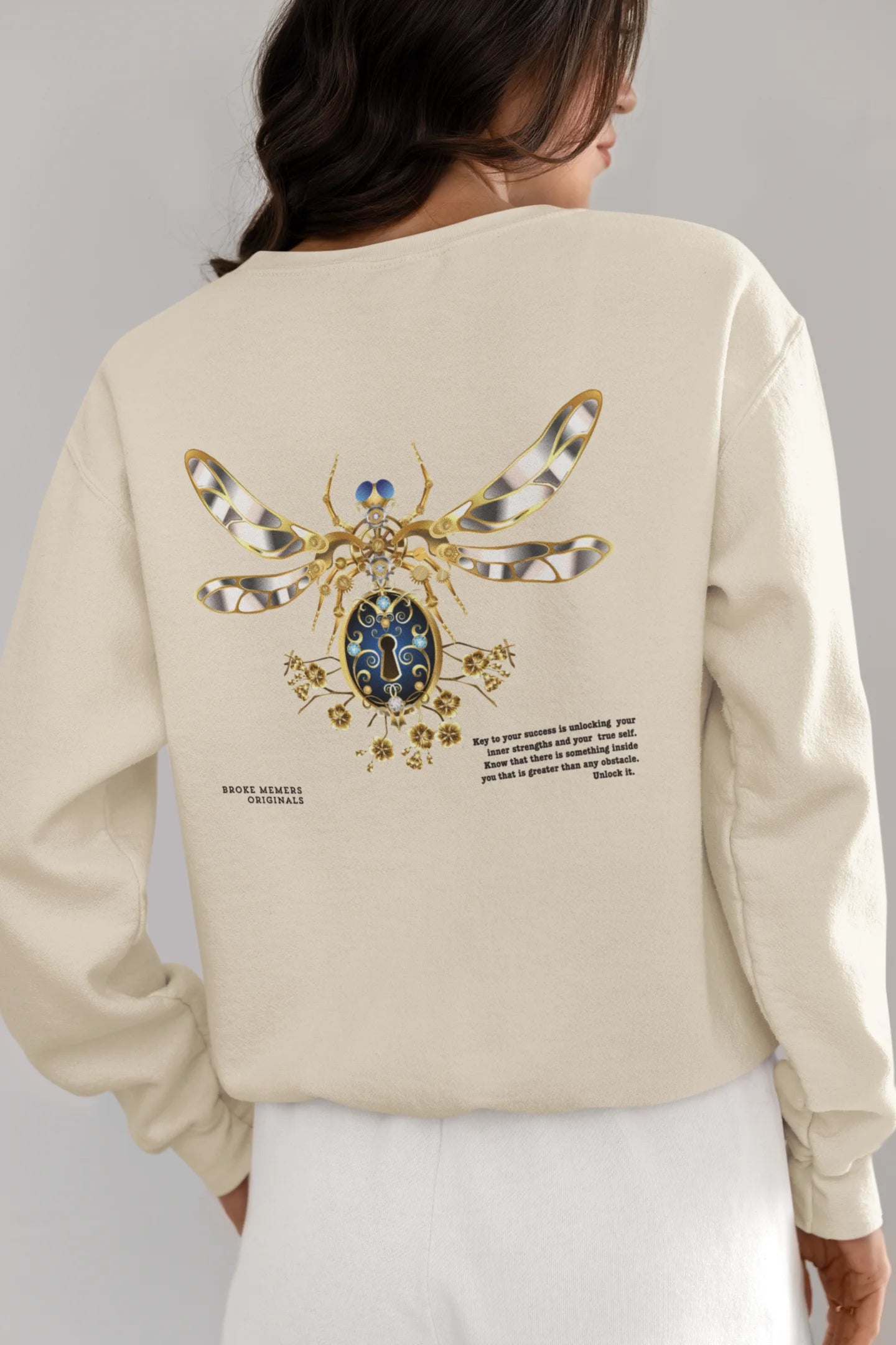 Back view of female model wearing an cream sweatshirt featuring a thought-provoking design of a golden lock shaped like an insect. Ideal for those who love symbolic clothing and unique conversation starters.
