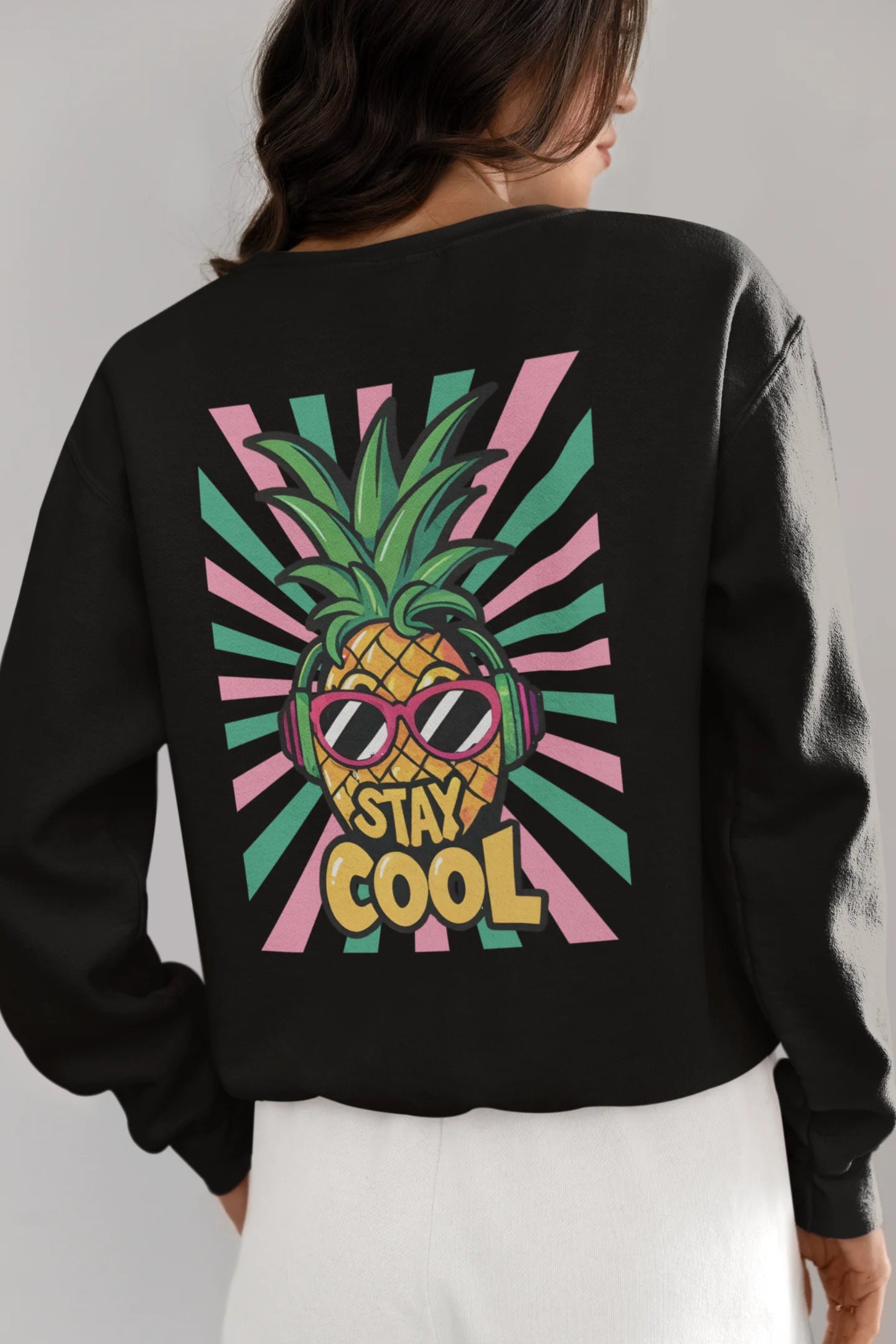 Back view of a female model wearing a trendy black sweatshirt featuring a pineapple wearing sunglasses with the slogan Stay Cool.