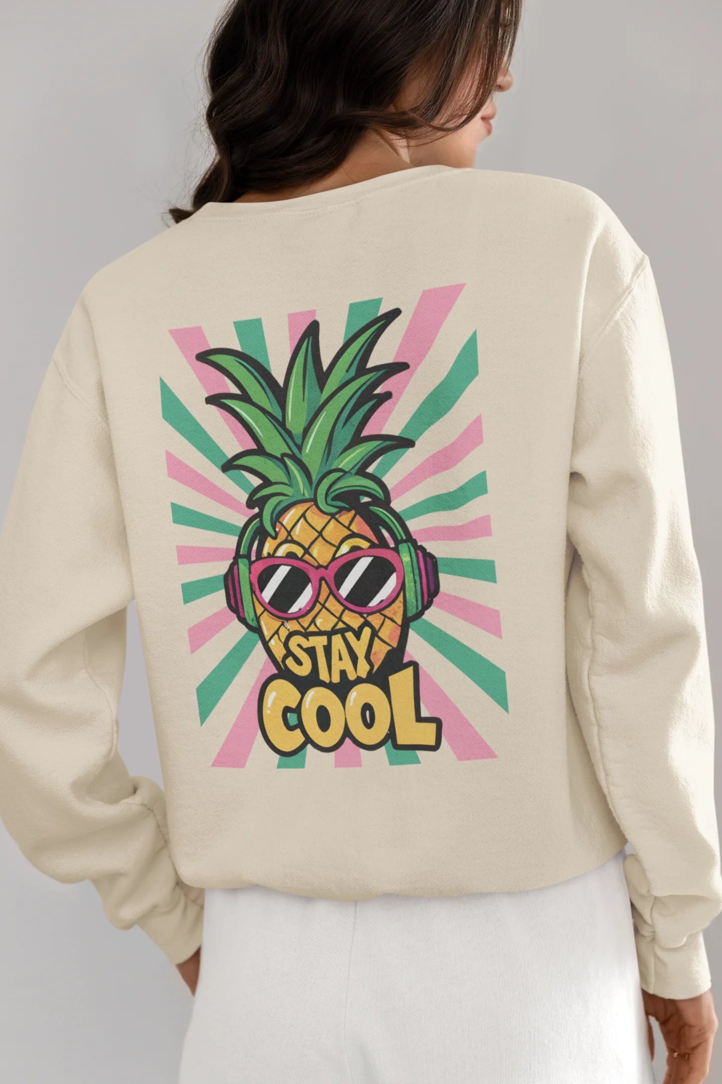 Back view of a female model wearing a trendy cream sweatshirt featuring a pineapple wearing sunglasses with the slogan Stay Cool.