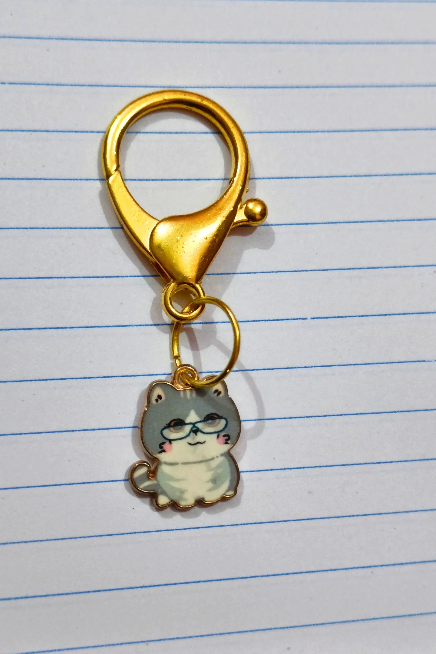A view of a couples keychain featuring two separate charms: one of a white cat wearing glasses.