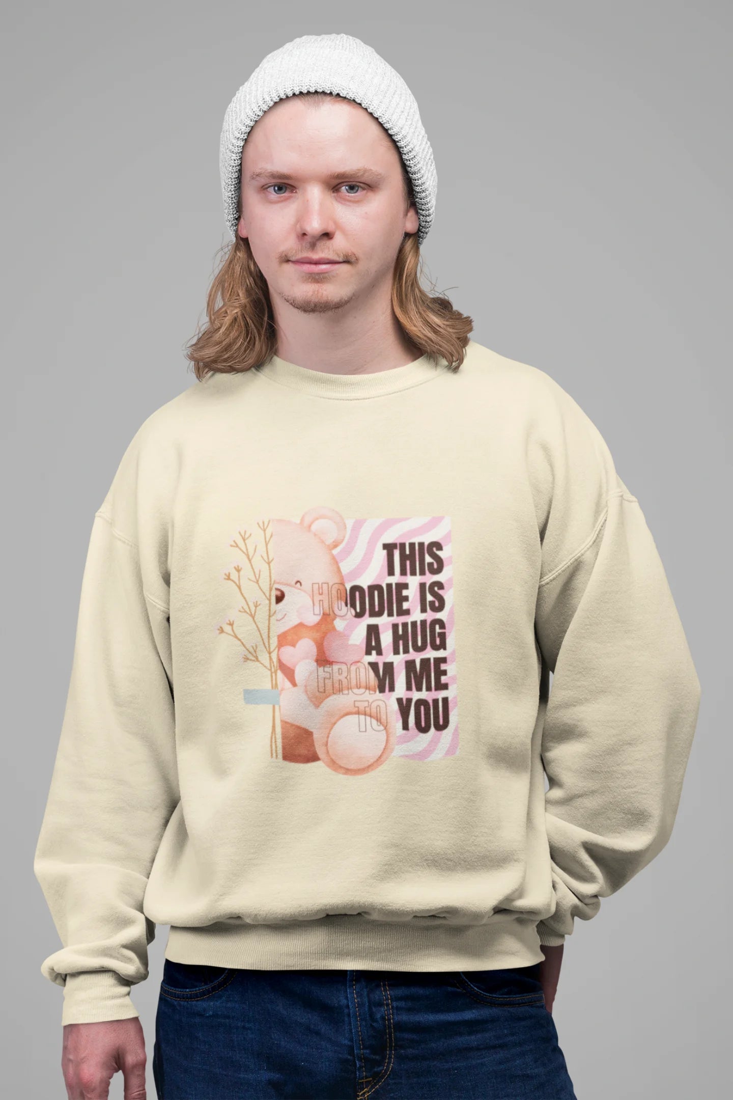 3rd front view of a male model wearing a cream sweatshirt with a heartwarming design of a teddy bear offering a hug, offering a comforting and relaxing aesthetic.