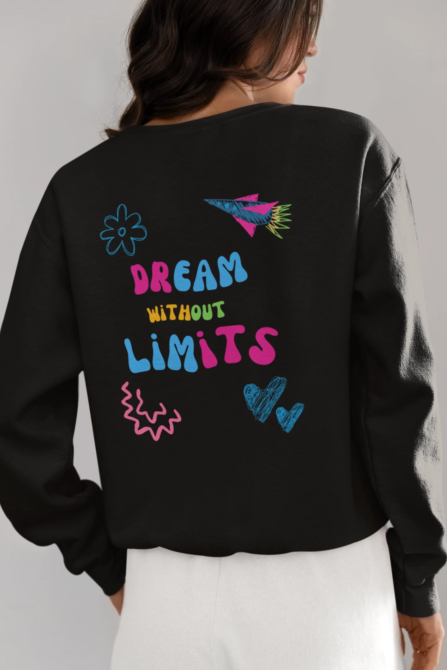 Back view of a female model wearing an black sweatshirt featuring colorful "Dream Without Limits" text, offering an inspiring and uplifting aesthetic.