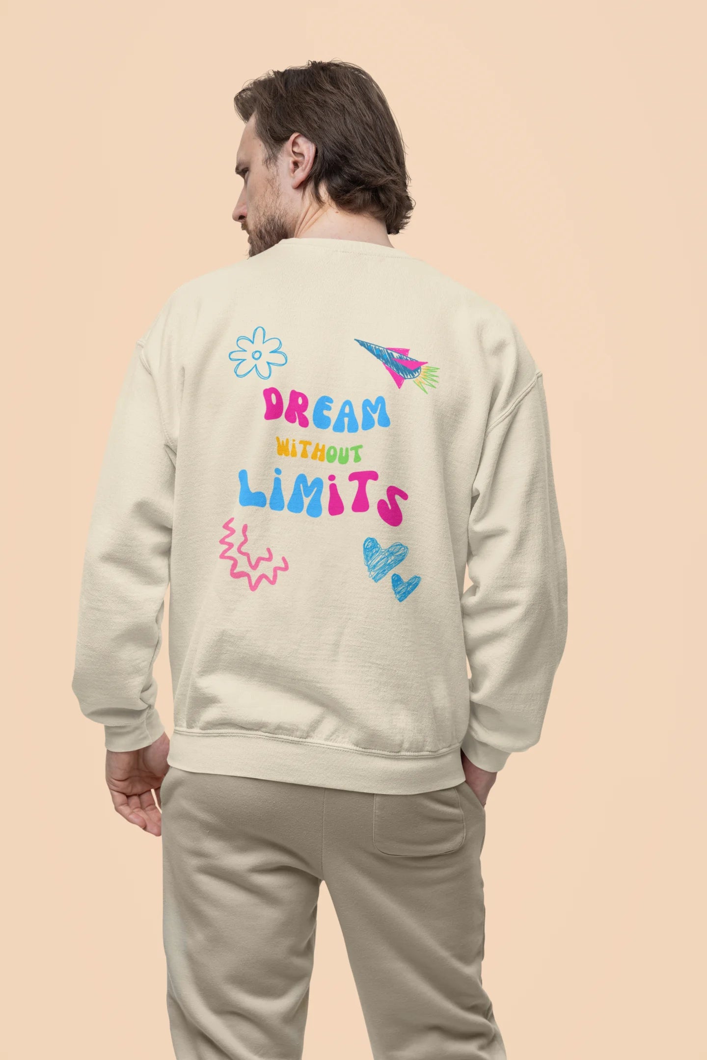 Back view of a male model wearing an cream sweatshirt featuring colorful "Dream Without Limits" text, offering an inspiring and uplifting aesthetic.