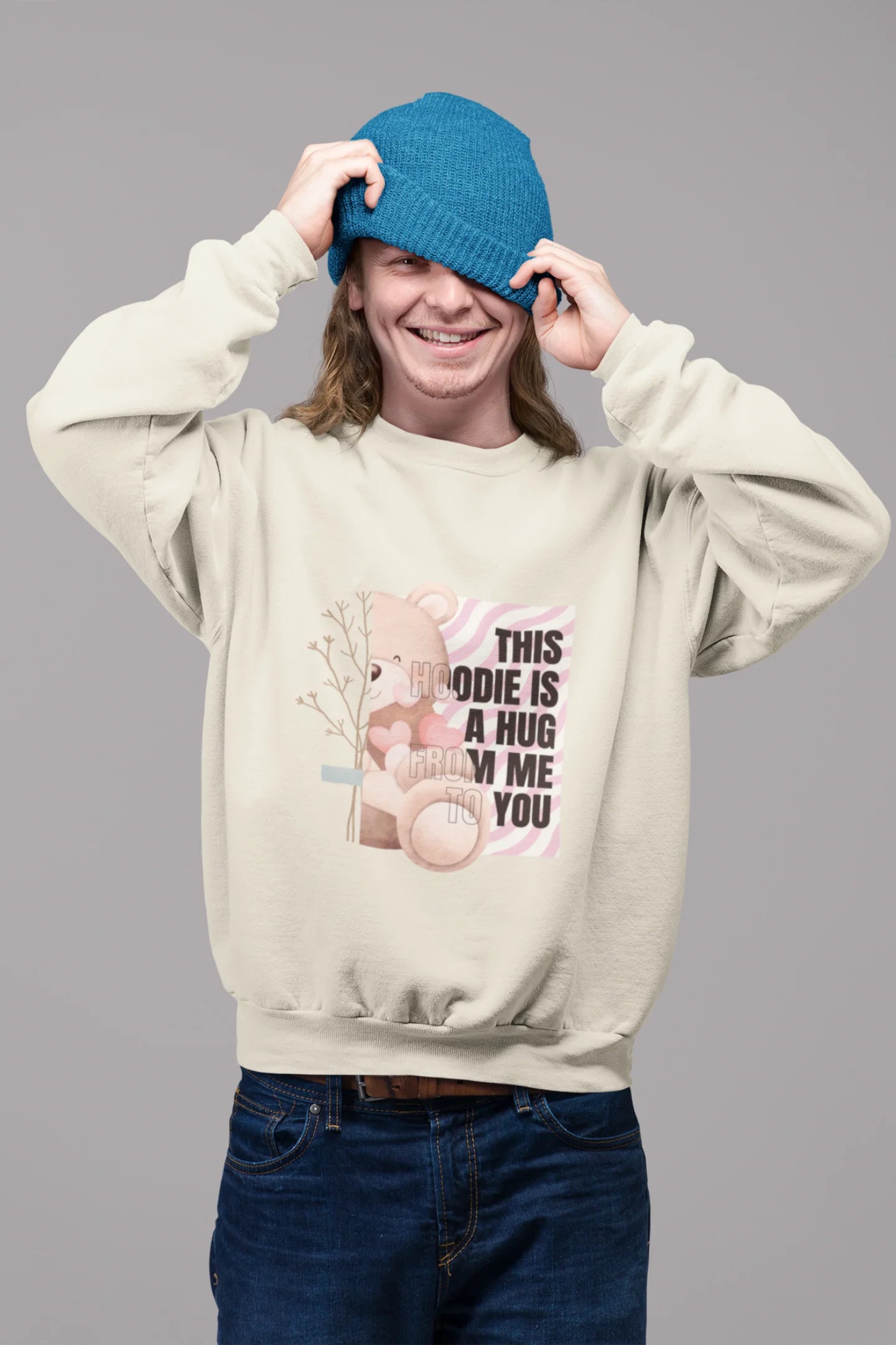 2nd front view of a male model wearing a cream sweatshirt with a heartwarming design of a teddy bear offering a hug, offering a comforting and relaxing aesthetic.