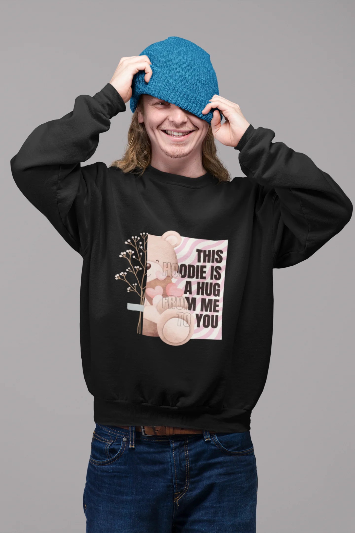 2nd front view of a male model wearing a black sweatshirt with a heartwarming design of a teddy bear offering a hug, offering a comforting and relaxing aesthetic.