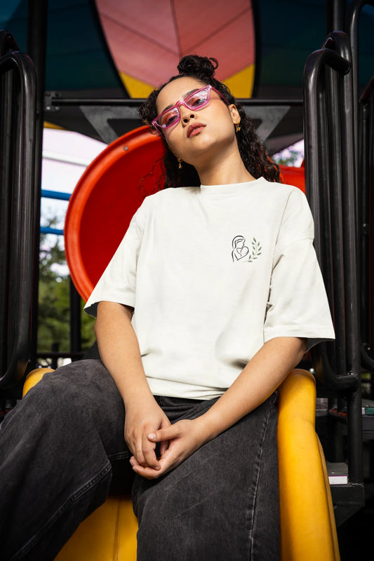 Front view of a female model wearing an off-white oversized t-shirt featuring a design depicting a mother tenderly holding a baby