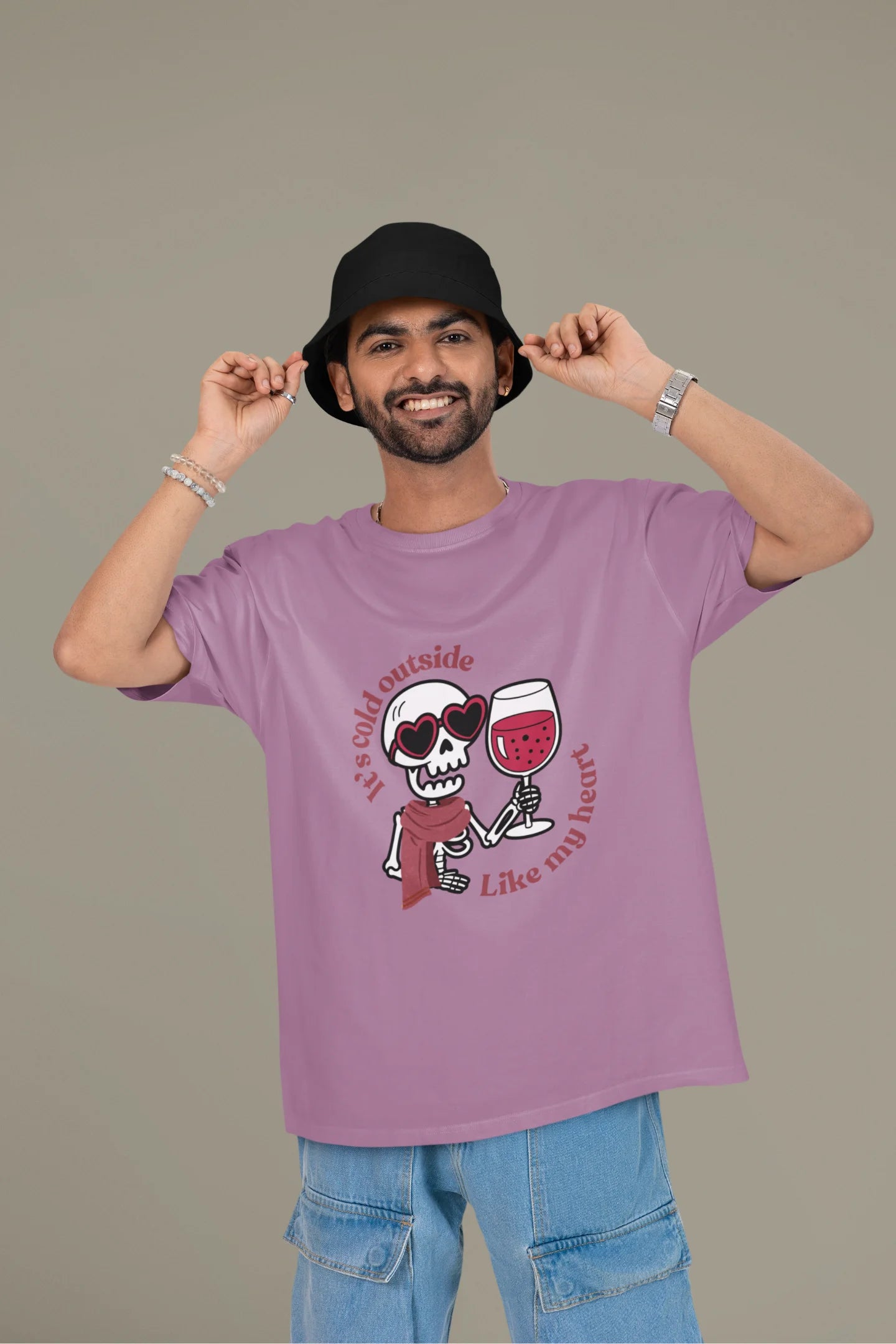2nd front image of a male model wearing a dirty purple oversized t-shirt with the text "Cold Outside Like My Heart" and a design of a skeleton drinking champagne.