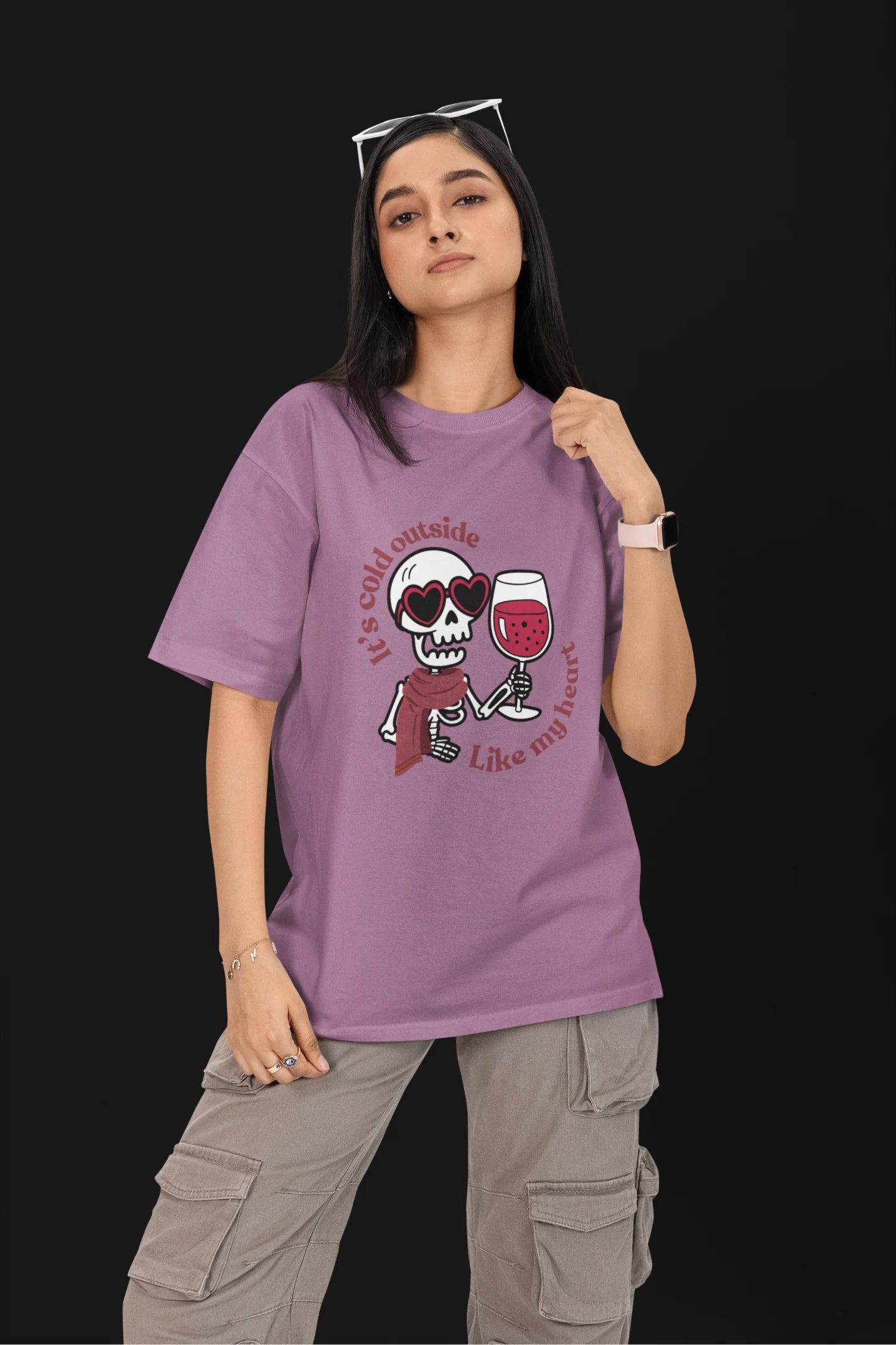 First front image of a female model wearing a dirty purple oversized t-shirt with the text "Cold Outside Like My Heart" and a design of a skeleton drinking champagne.
