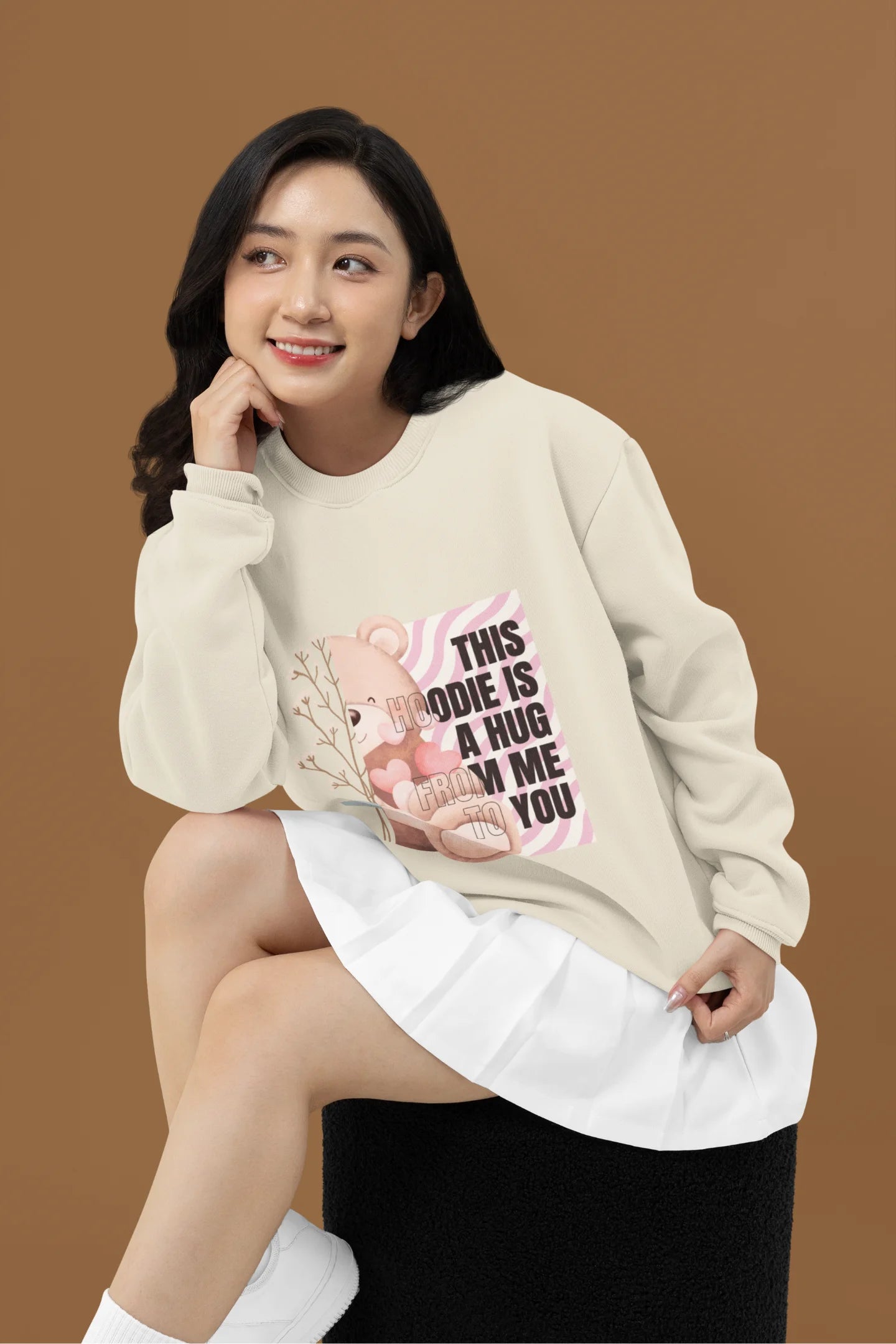 2nd front view of a female model wearing a cream sweatshirt with a heartwarming design of a teddy bear offering a hug, offering a comforting and relaxing aesthetic.
