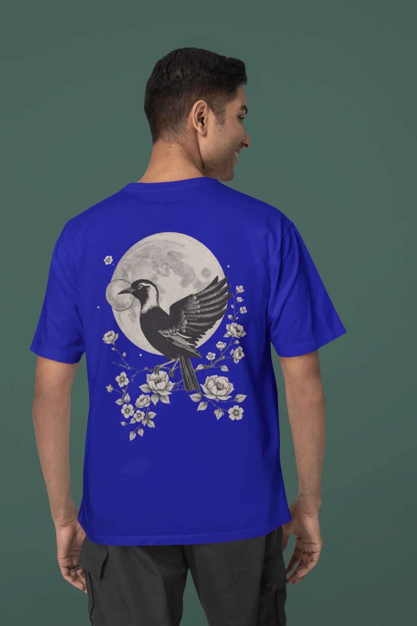 Back view of a male model wearing a royal blue oversized tee with a heron taking off under the moonlight.