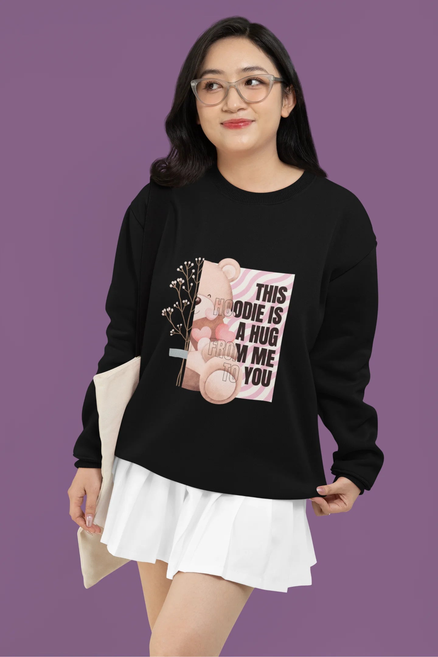 First front view of a female model wearing a black sweatshirt with a heartwarming design of a teddy bear offering a hug, offering a comforting and relaxing aesthetic.