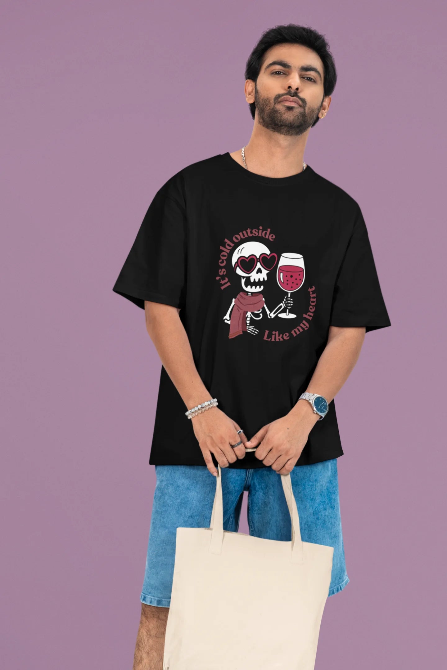 First front image of a male model wearing a black oversized t-shirt with the text "Cold Outside Like My Heart" and a design of a skeleton drinking champagne.