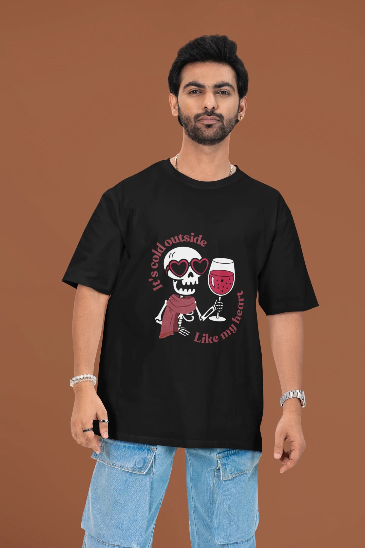 3rd front image of a male model wearing a black oversized t-shirt with the text "Cold Outside Like My Heart" and a design of a skeleton drinking champagne.
