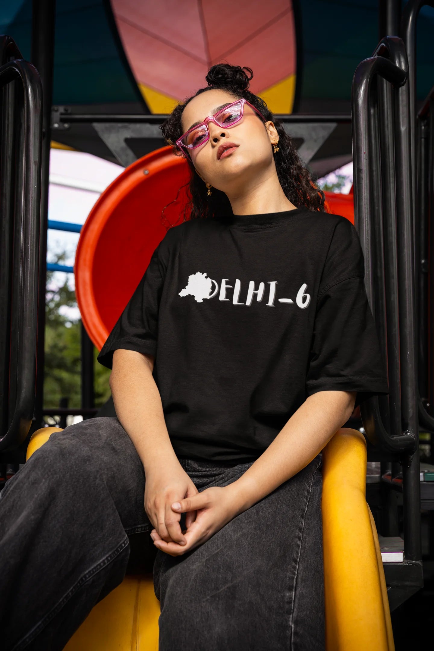 Front view of a female model wearing a black oversized t-shirt featuring a design incorporating the Red Fort and elements representing the city of Delhi, inspired by the Hindi film Delhi 6.