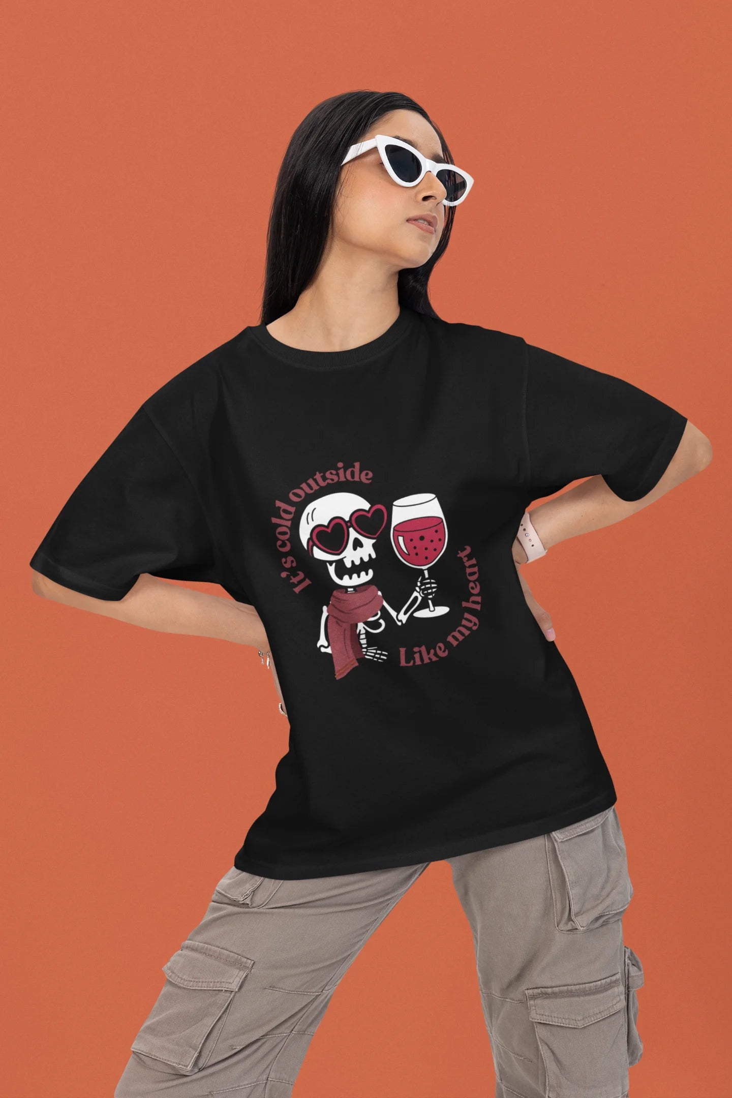 2nd front image of a female model wearing a black oversized t-shirt with the text "Cold Outside Like My Heart" and a design of a skeleton drinking champagne.
