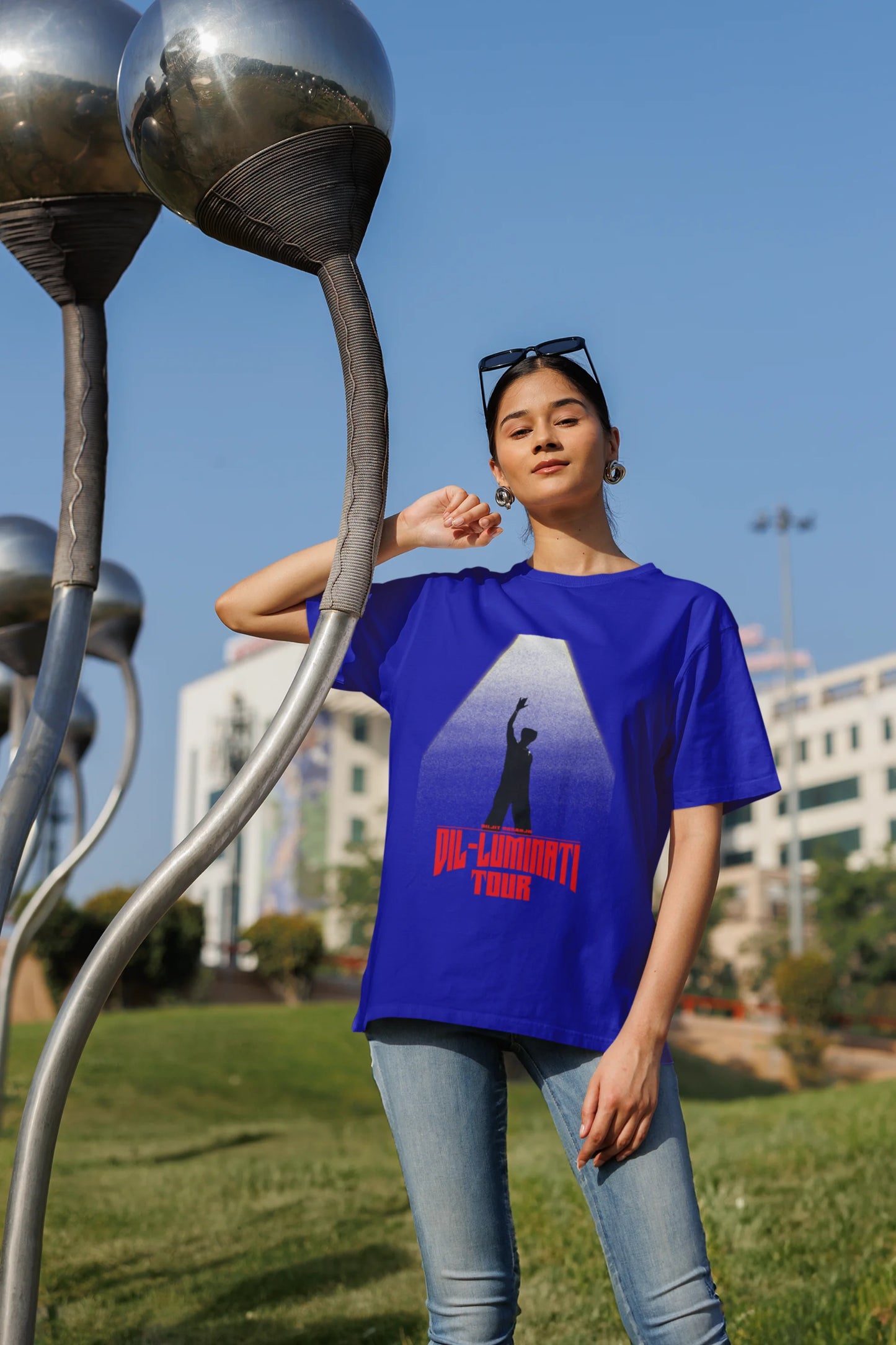 Fourth front view of a female model wearing a royal blue oversized t-shirt with a portrait of Diljit Dosanjh on stage, bathed in the warm glow of a spotlight.
