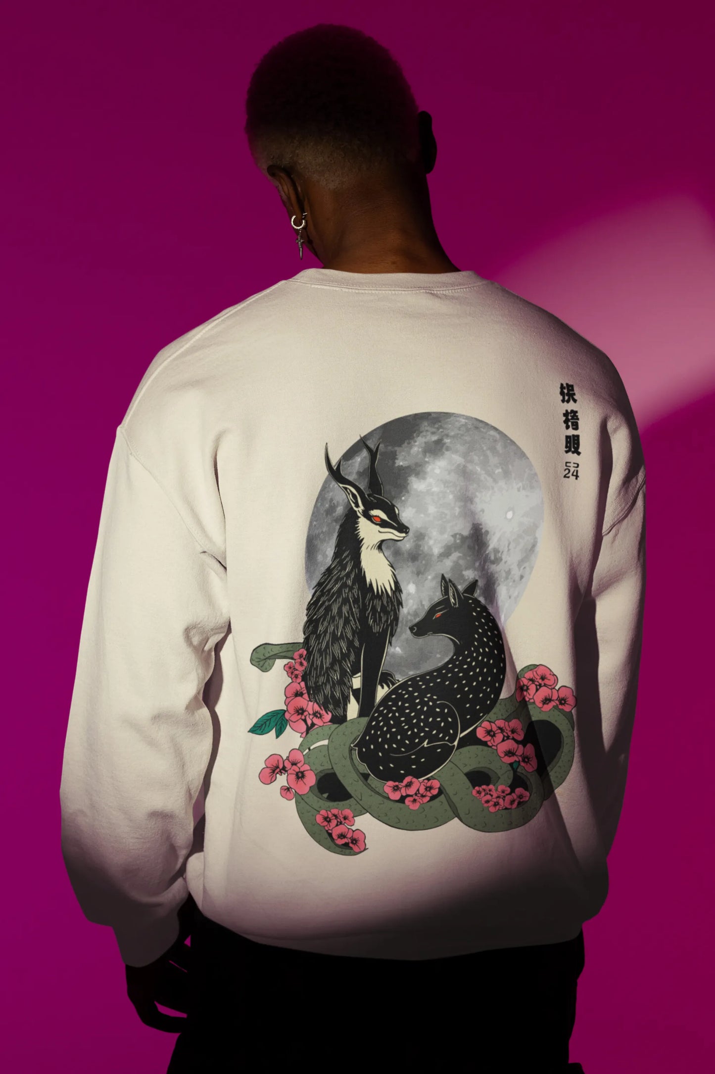 Back view of a male model wearing an cream sweatshirt featuring a detailed illustration of a gray wolf howling at a full moon in a nighttime setting.