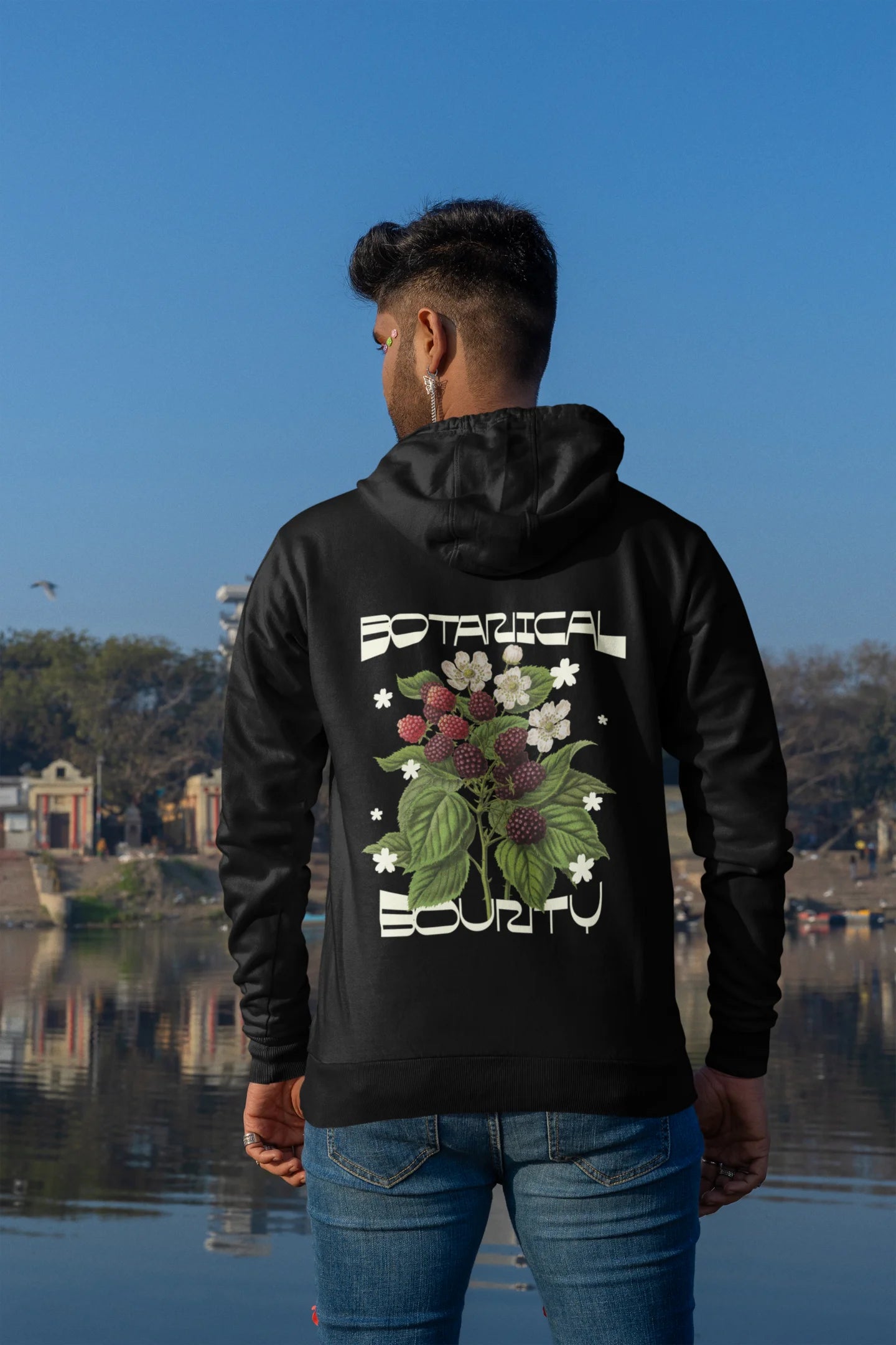 Back view of a male model model wearing a black hoodie with a design featuring berry bushes overflowing with fruit, symbolizing the abundance and beauty of nature.