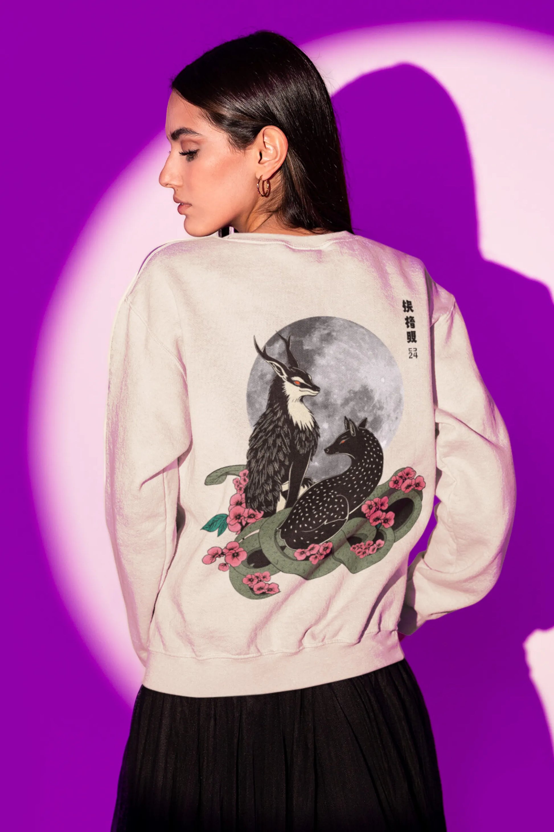Back view of a female model wearing an cream sweatshirt featuring a detailed illustration of a gray wolf howling at a full moon in a nighttime setting.