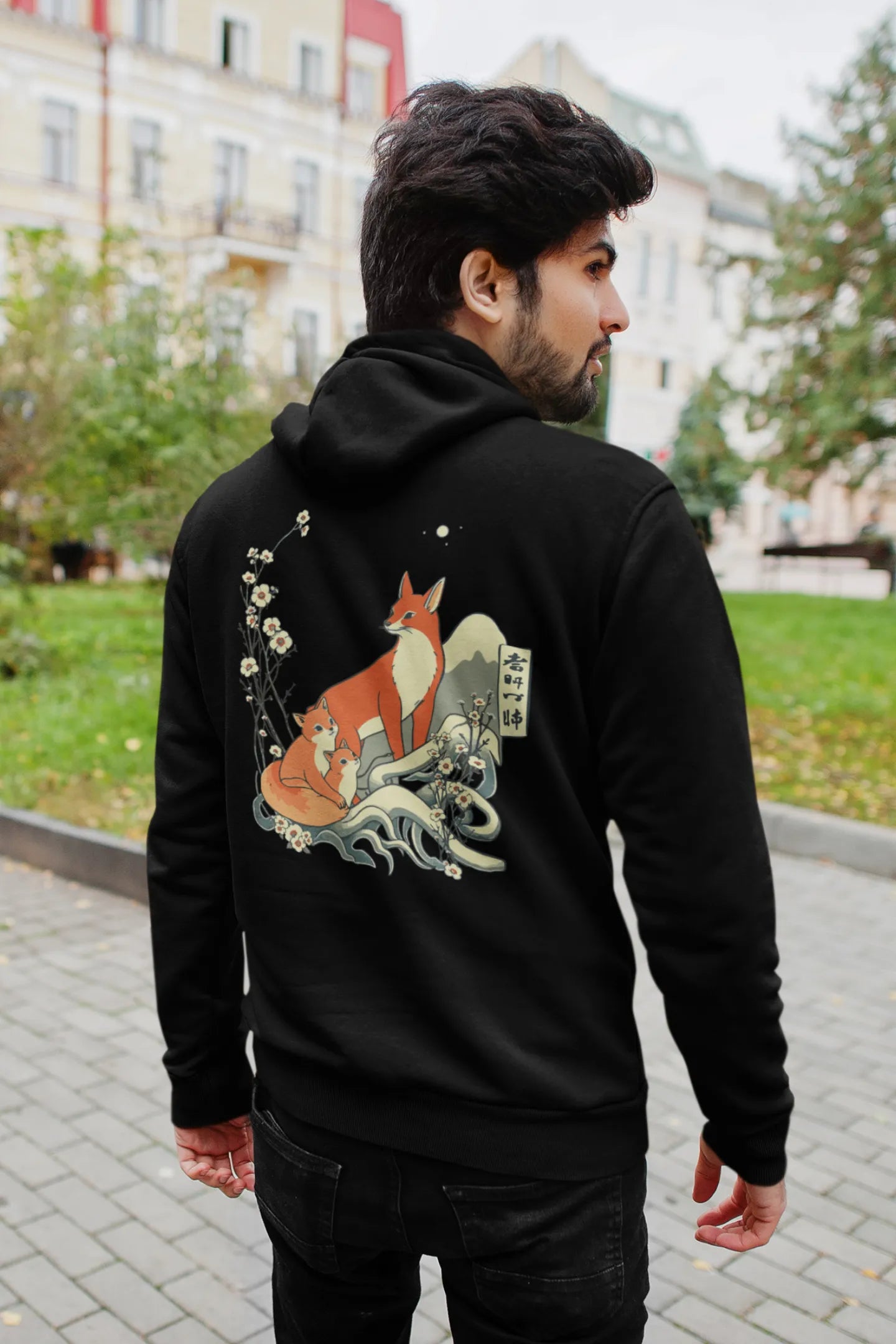 First front of a male model wearing a black hoodie with a design of a fox and its cub in a traditional Japanese landscape.