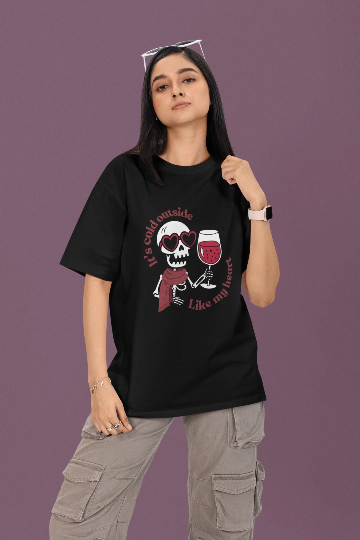 First front image of a female model wearing a black oversized t-shirt with the text "Cold Outside Like My Heart" and a design of a skeleton drinking champagne.