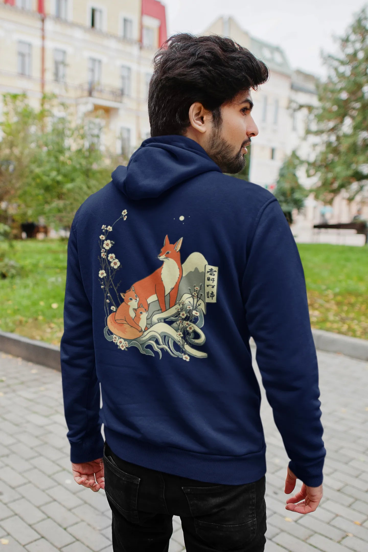 Back view male model wearing a navy blue hoodie with a design of a fox and its cub in a traditional Japanese landscape.
