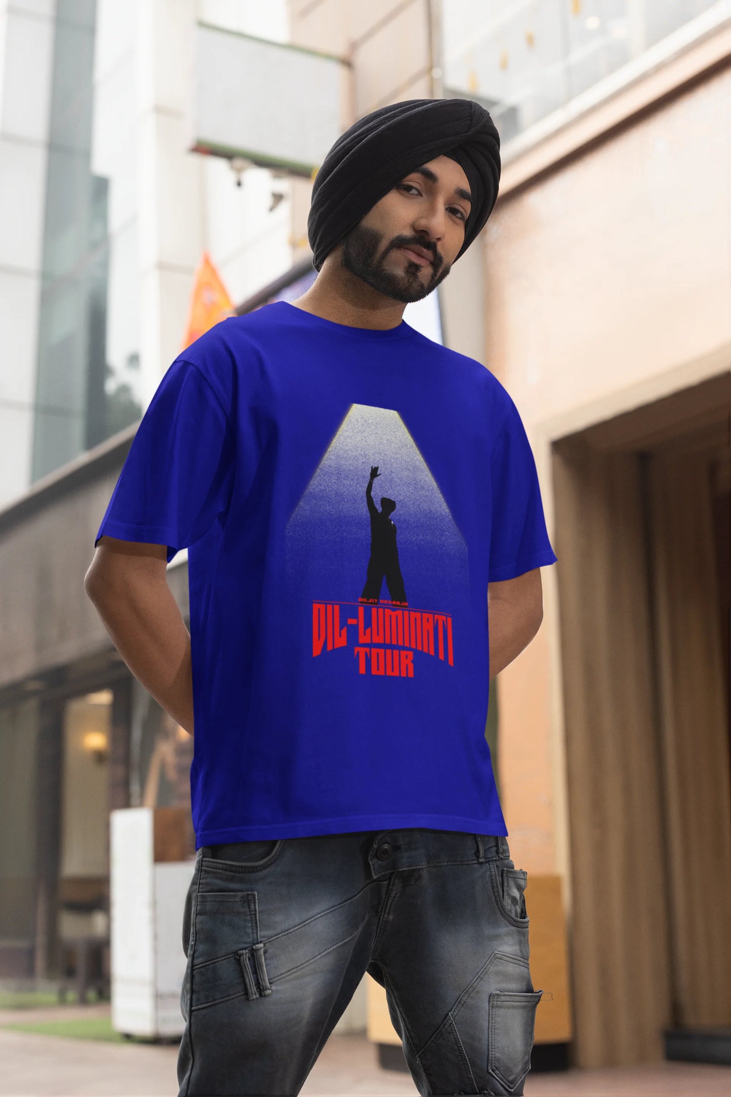 Second front view of a male model wearing a royal blue oversized t-shirt with a portrait of Diljit Dosanjh on stage, bathed in the warm glow of a spotlight.