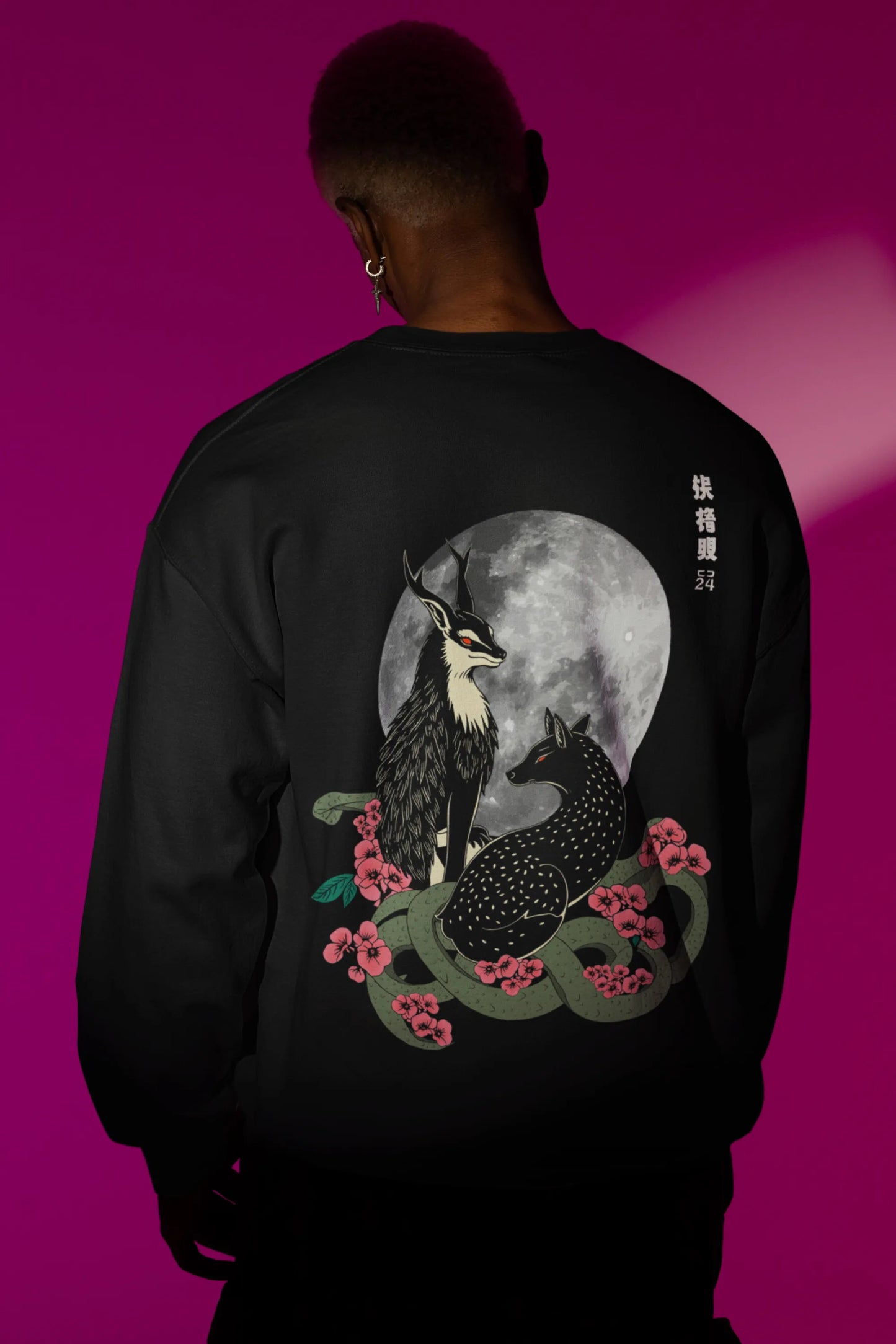 Back view of a male model wearing an black sweatshirt featuring a detailed illustration of a gray wolf howling at a full moon in a nighttime setting.