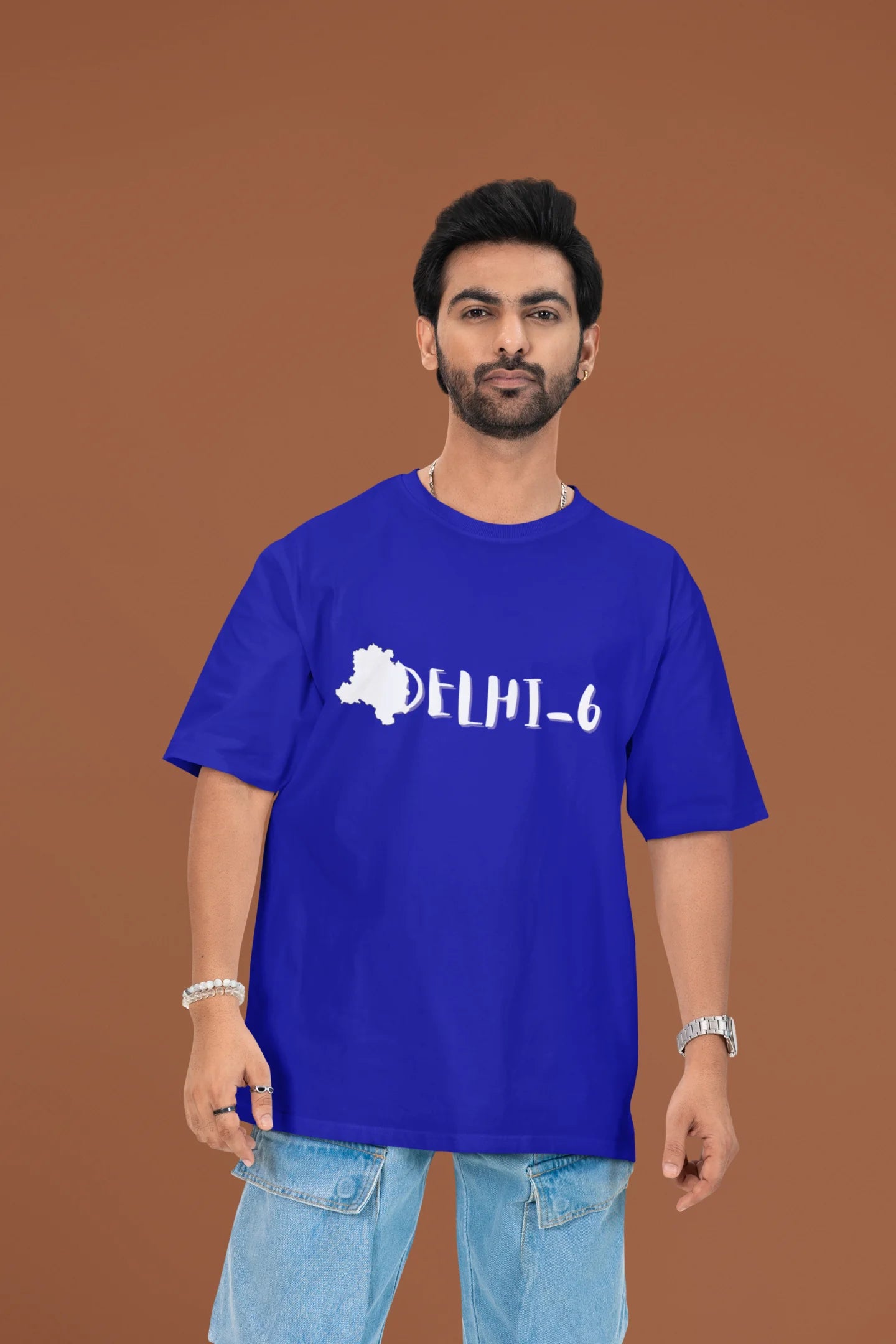 Another front view of a male model wearing a royal blue oversized t-shirt featuring a design incorporating the Red Fort and elements representing the city of Delhi, inspired by the Hindi film Delhi 6.