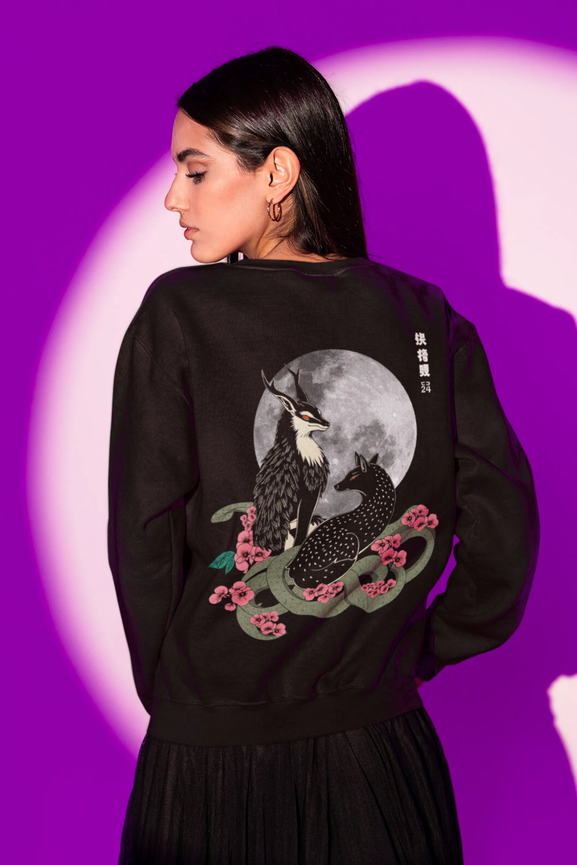 Back view of a female model wearing an cream sweatshirt featuring a detailed illustration of a gray wolf howling at a full moon in a nighttime setting.