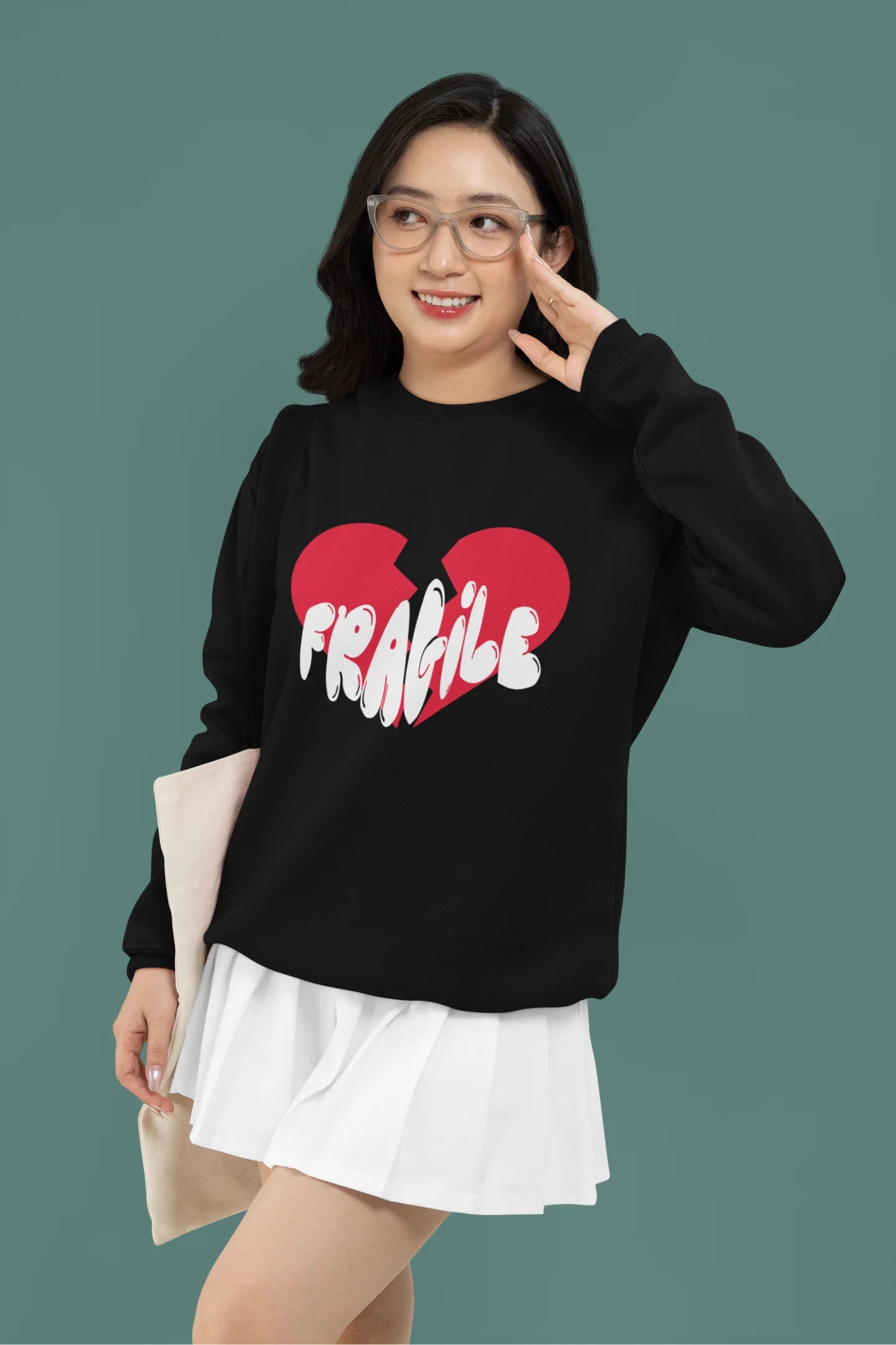 First front view of a female model wearing a black sweatshirt with a broken heart design and the word "Fragile" in melting text.