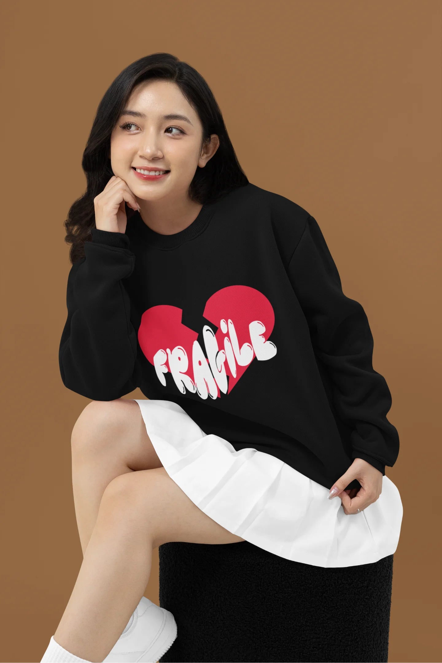 2nd front view of a female model wearing a black sweatshirt with a broken heart design and the word "Fragile" in melting text.