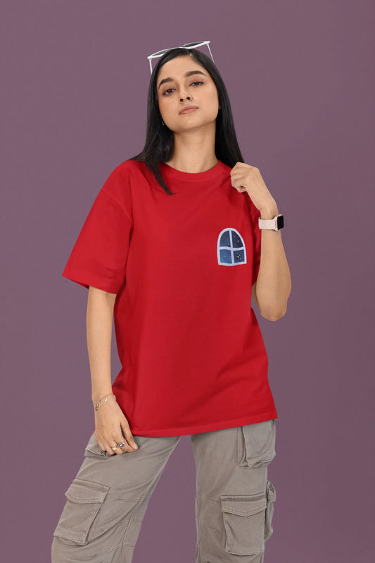 First front view of a female model wearing a red oversized t-shirt featuring an illustration called Mithi Neend of children lying or sitting on a rooftop, looking up at a starry night sky.