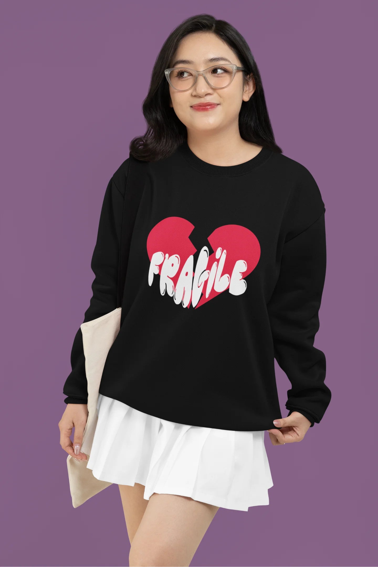 3rd front view of a female model wearing a black sweatshirt with a broken heart design and the word "Fragile" in melting text.