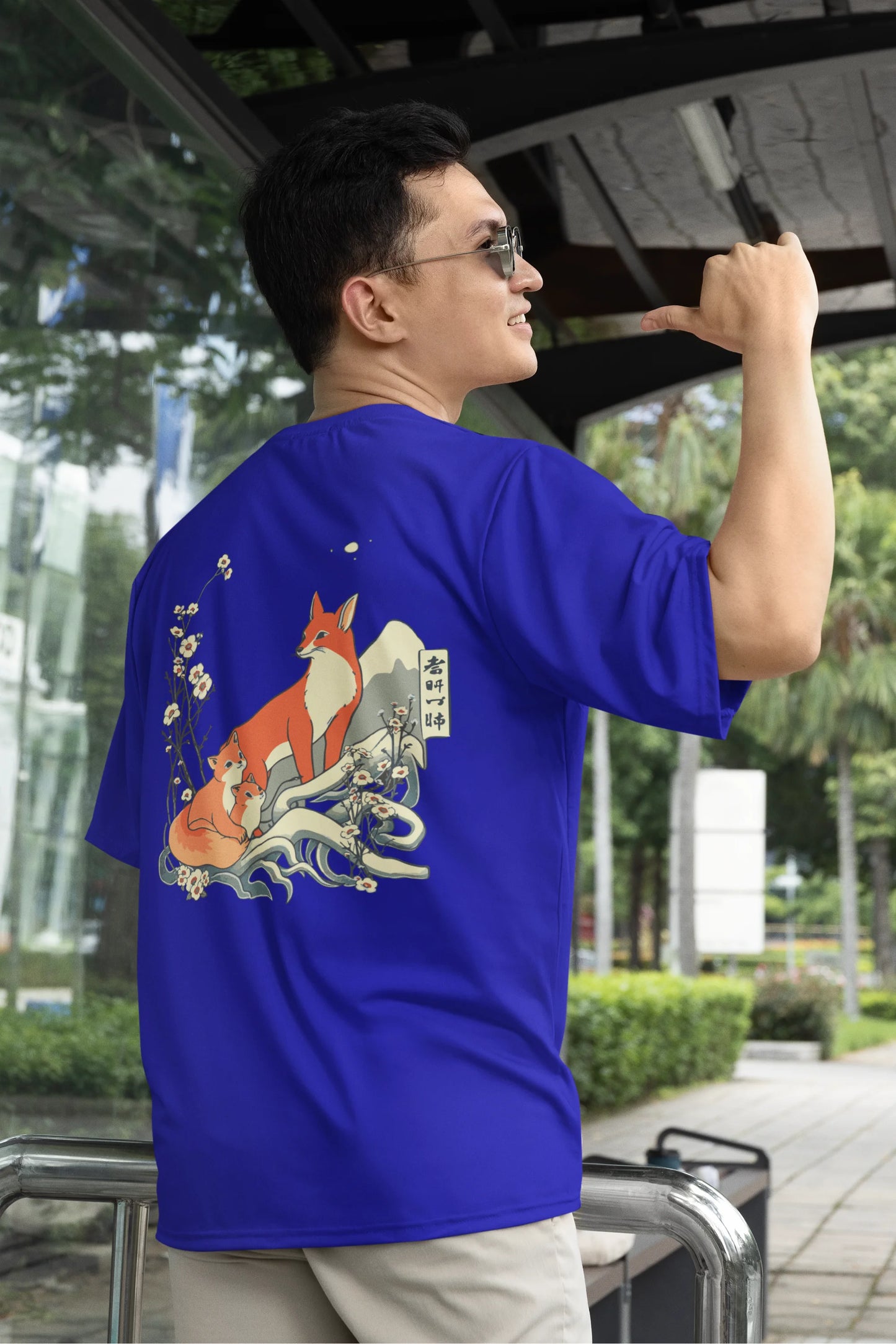 First back view of a male model wearing a royal blue oversized tee with a design of a fox and its cub in a traditional Japanese landscape.