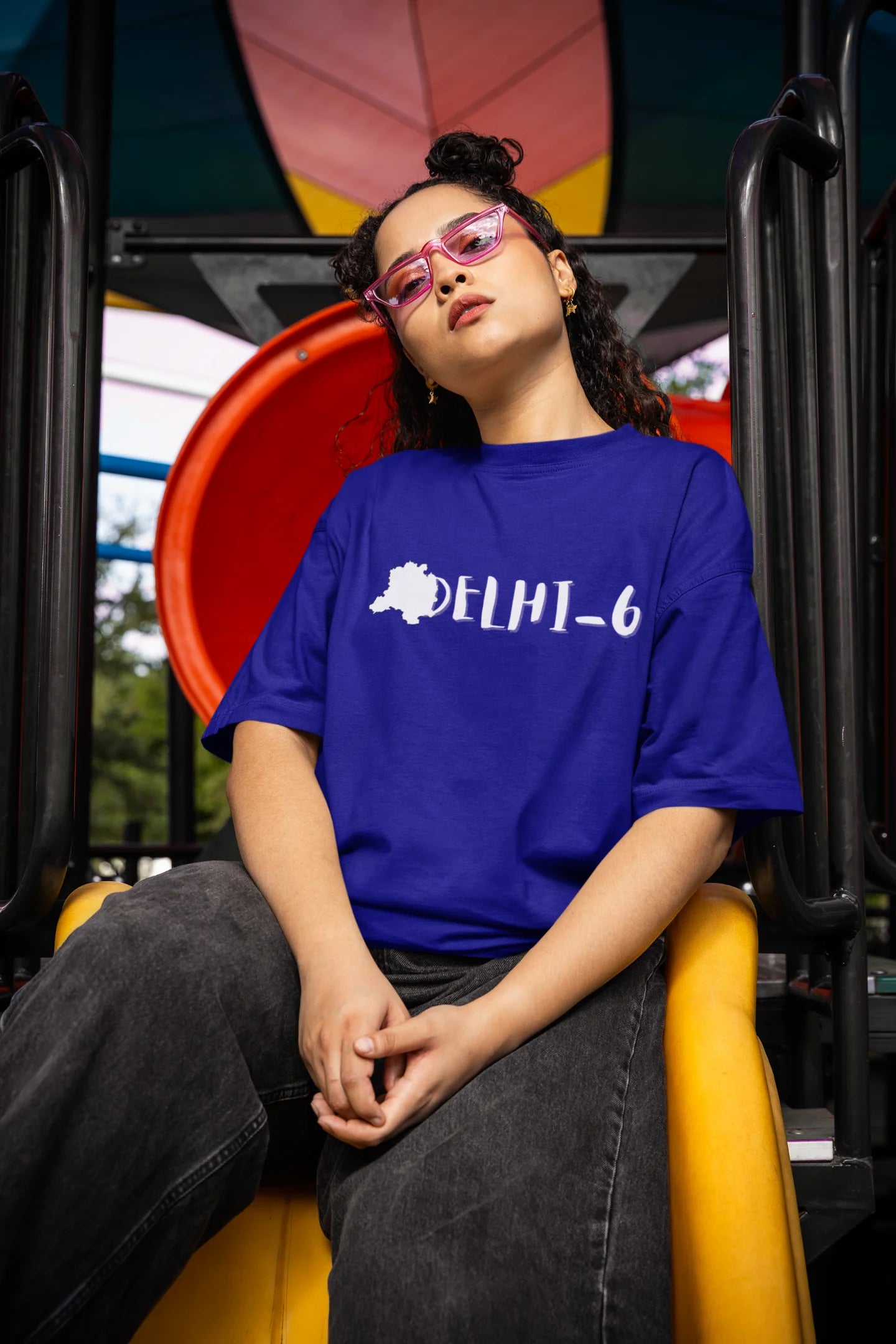 Front view of a female model wearing a royal blue oversized t-shirt featuring a design incorporating the Red Fort and elements representing the city of Delhi, inspired by the Hindi film Delhi 6.