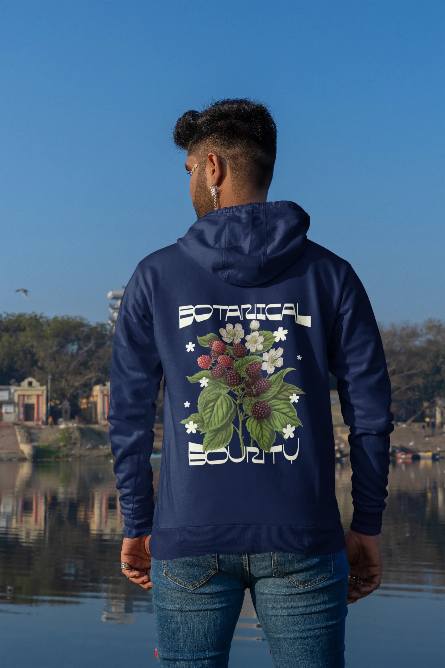 Back of a male model model wearing a navy hoodie with a design featuring berry bushes overflowing with fruit, symbolizing the abundance and beauty of nature.
